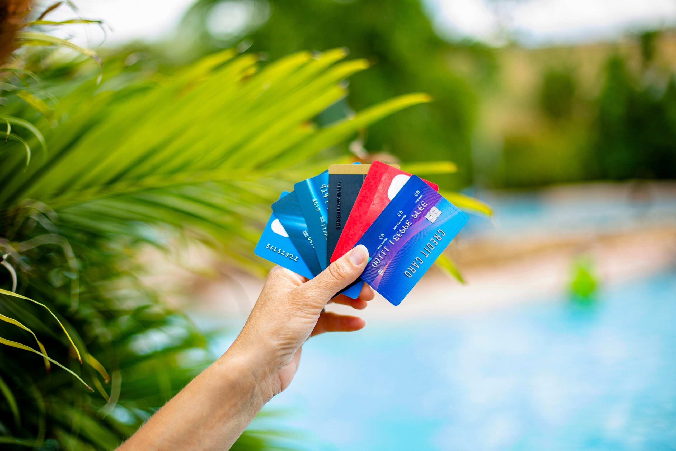 Holding a handful of credit cards used to pay for a fun trip to a beautiful tropical destination. Travel concept photo of a woman holding credit cards with a island resort in the background.