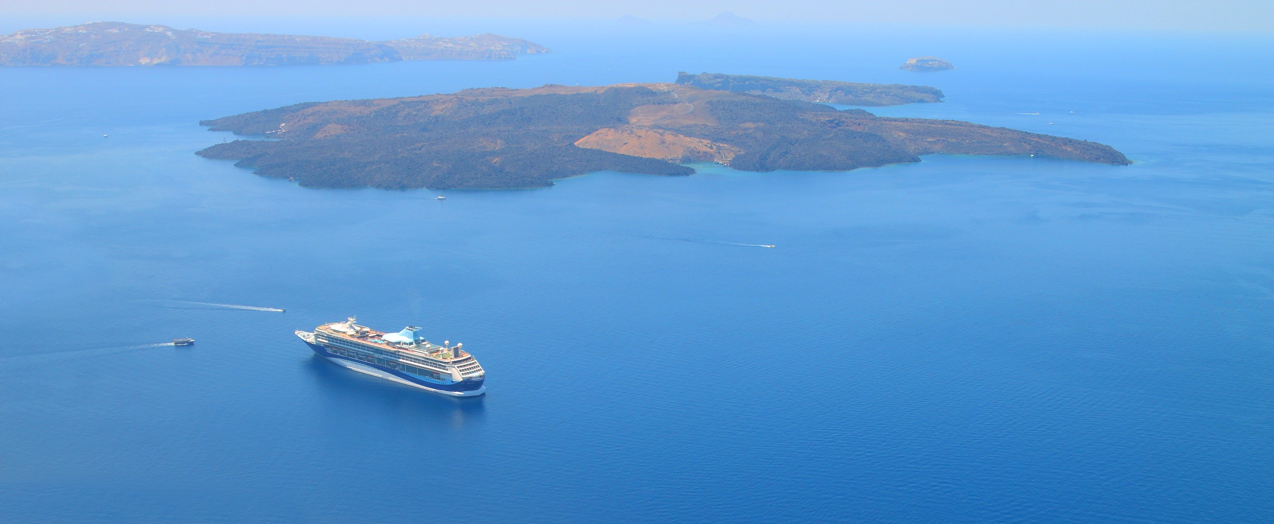 Santorini, Greece, a panoramic view of a giant cruise ship anchored in front of the ancient volcano crater of the greek island
