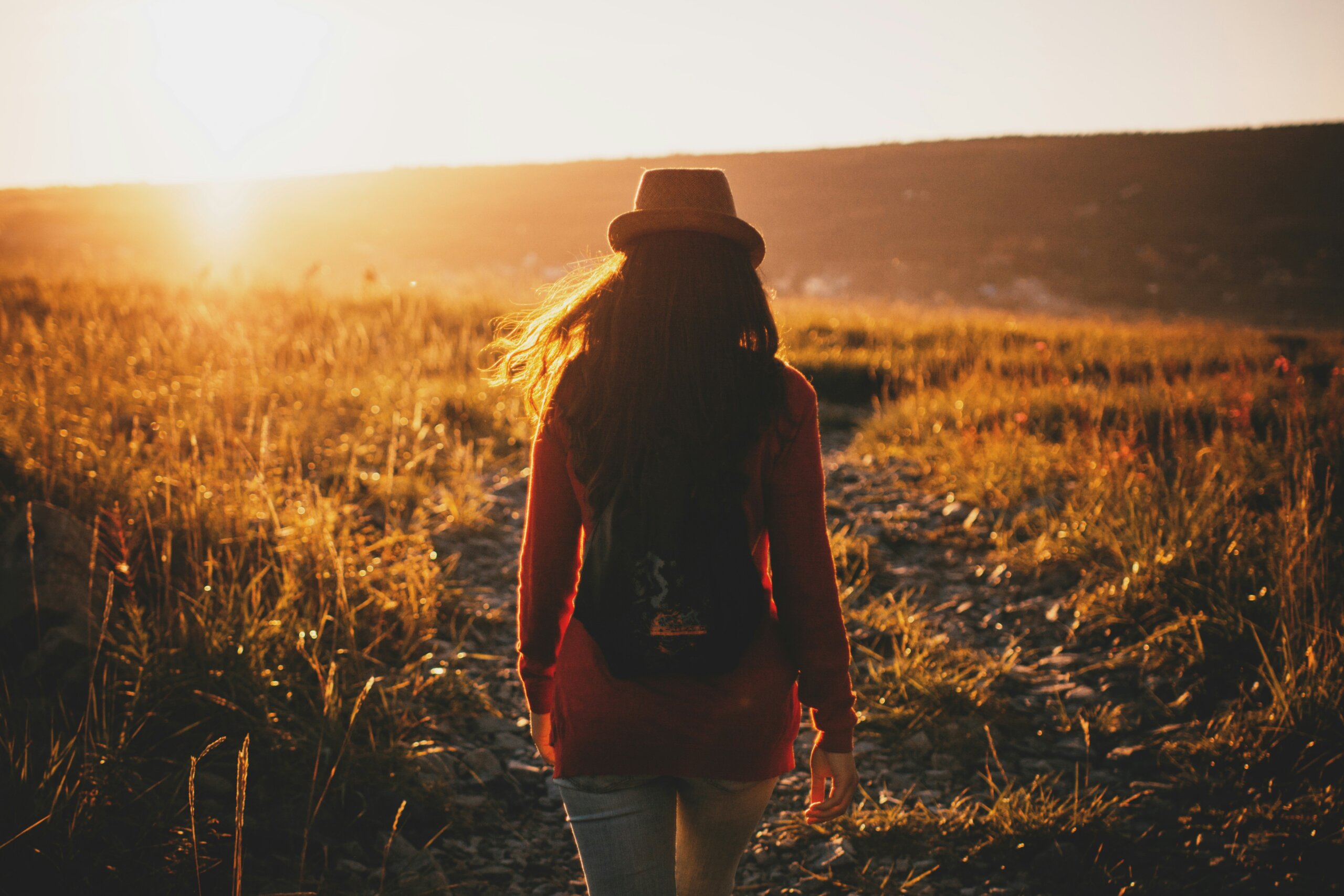 Woman walking alone on a golden trail at sunset, symbolizing solo travel and gratitude during Thanksgiving.