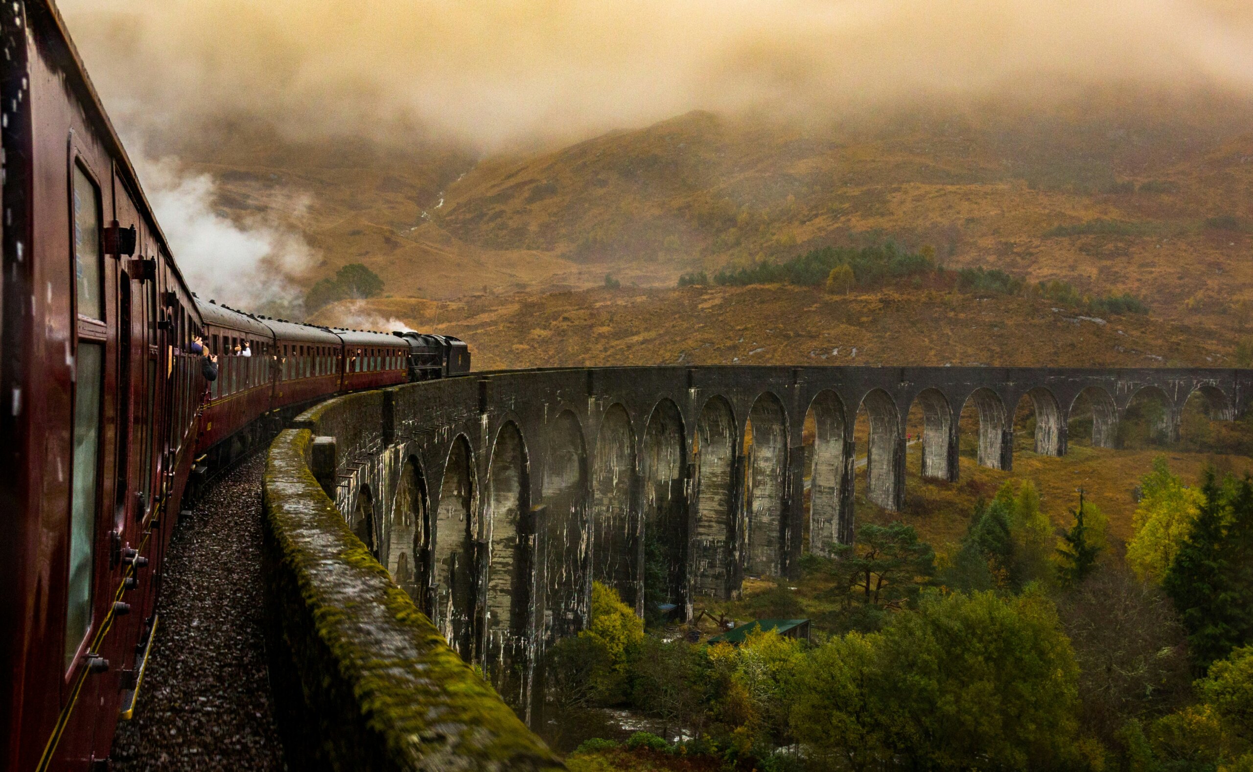 Red train crossing a scenic viaduct in the misty Scottish Highlands symbolizing the return of train travel and slow travel movement.