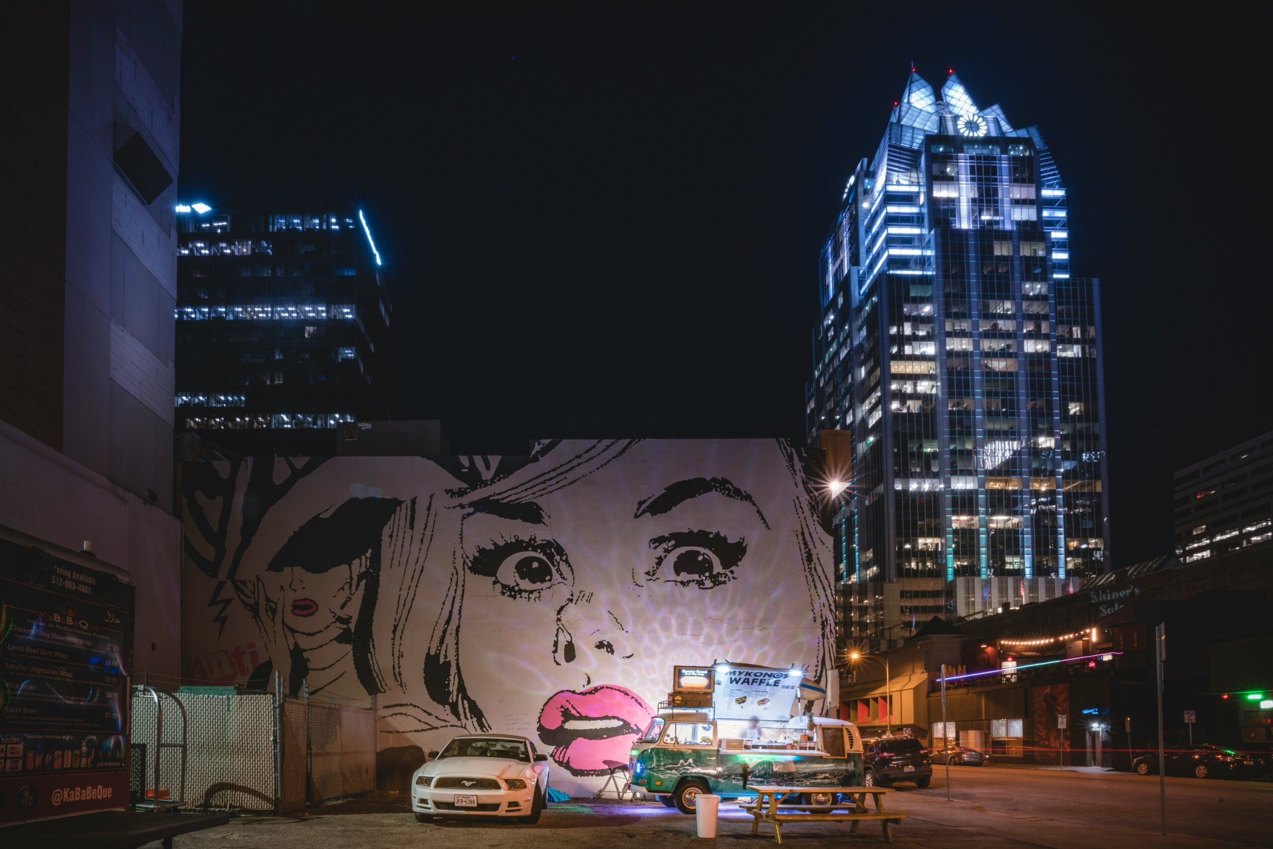 Downtown Austin skyline at night with illuminated buildings and large street art mural, symbolizing a city feeling the pressures of change.