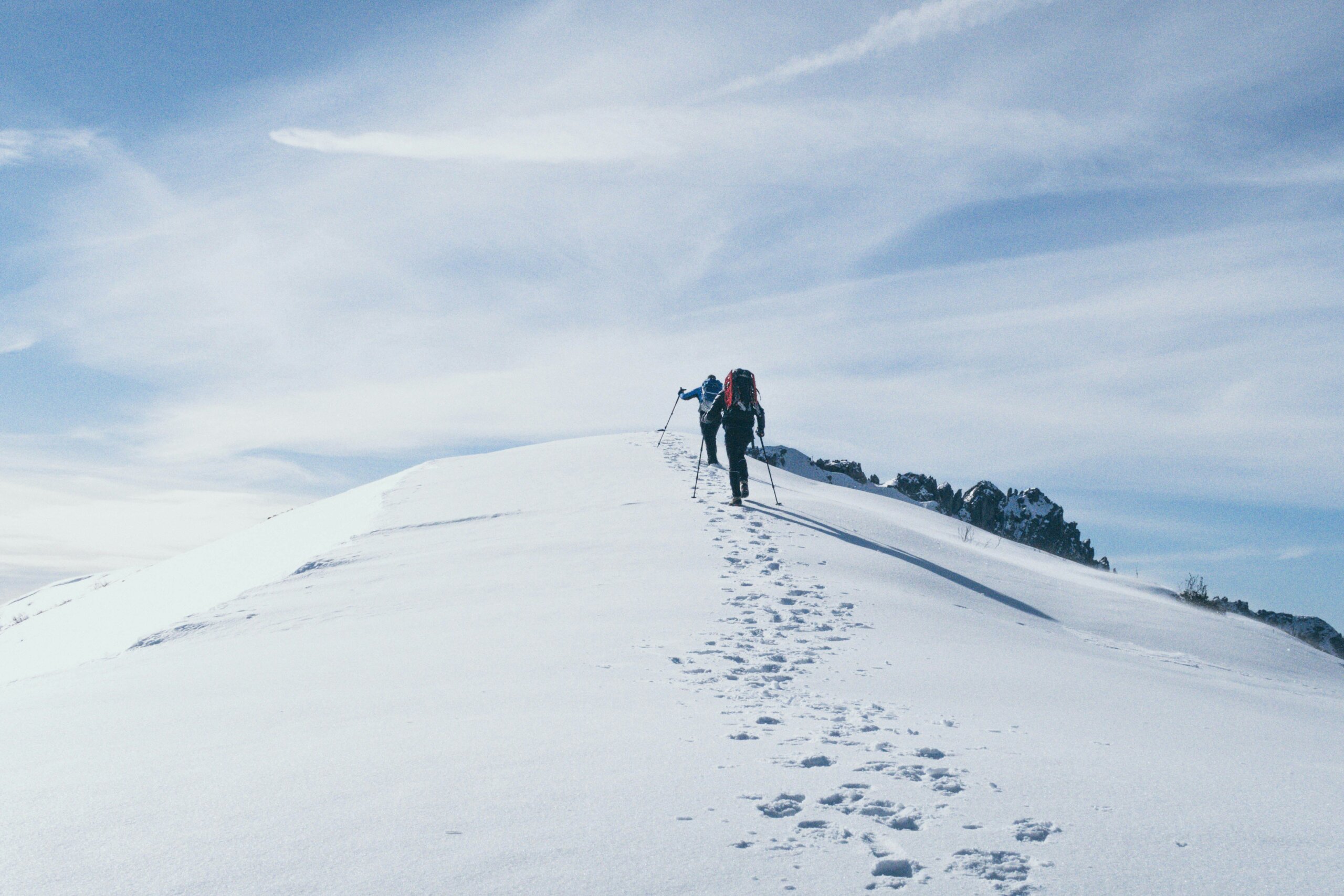 Hikers trekking across snowy mountain ridge under blue sky, symbolizing stunning winter hikes in the U.S.