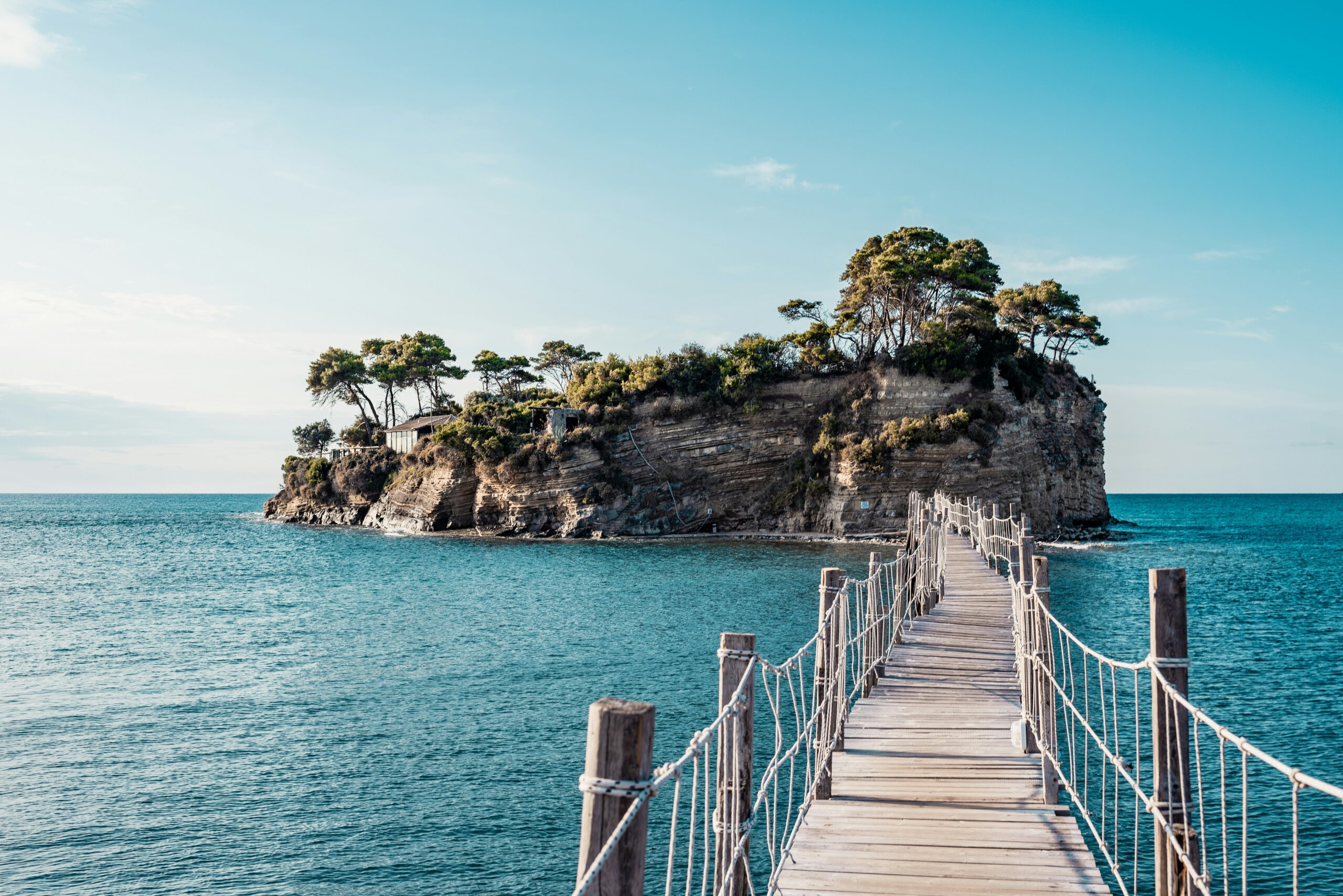 Wooden bridge leading to a small island over turquoise water on a sunny day.