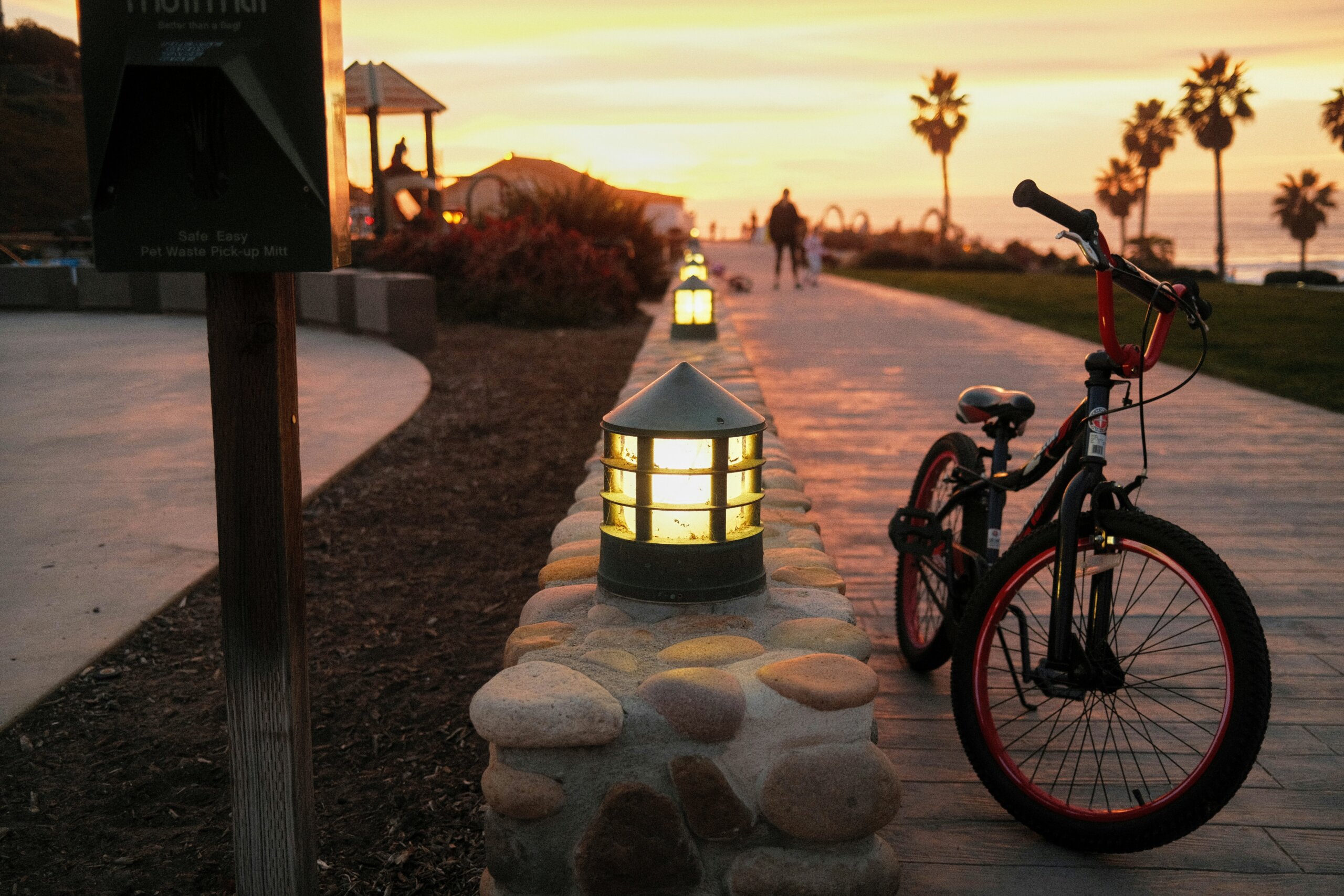 Coastal bike path at sunset with lantern lights and palm trees, symbolizing peaceful living in one of the safest and most affordable cities.
