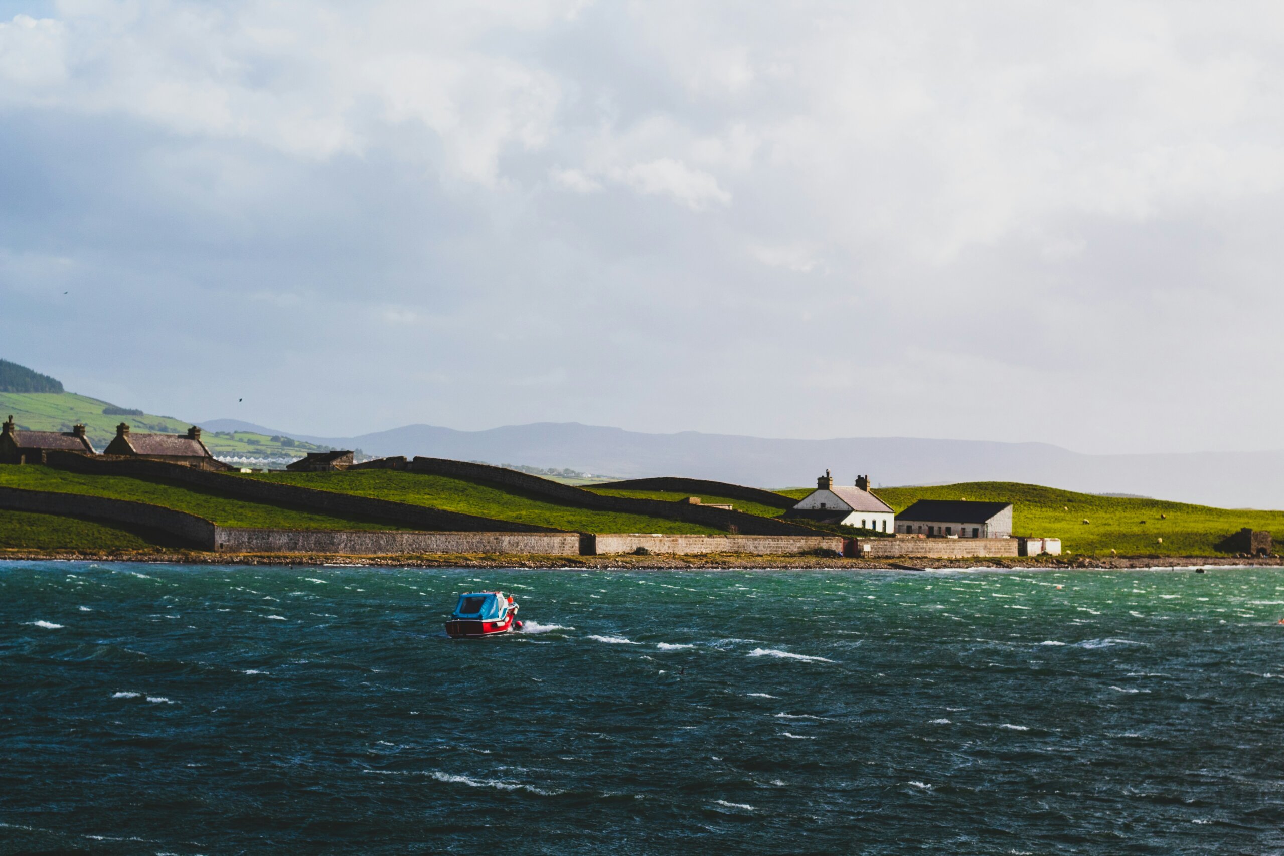 Sligo coastline with small red boat on the water and green fields in the background, showcasing Ireland’s wild beauty and Yeats Country.
