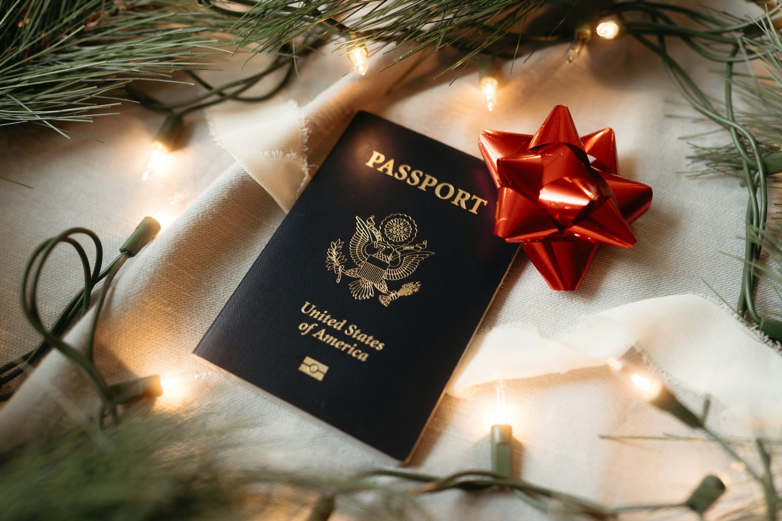 Holiday-themed U.S. passport with red bow and pine branches symbolizing 2025 travel planning and booking tips.