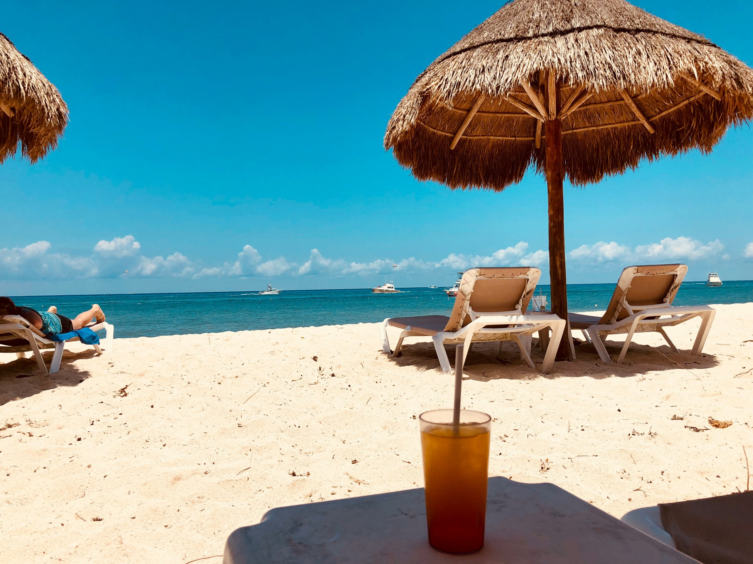 Beach chairs under a thatched umbrella on a tropical shoreline, representing affordable beachside living for $2,000 a month.