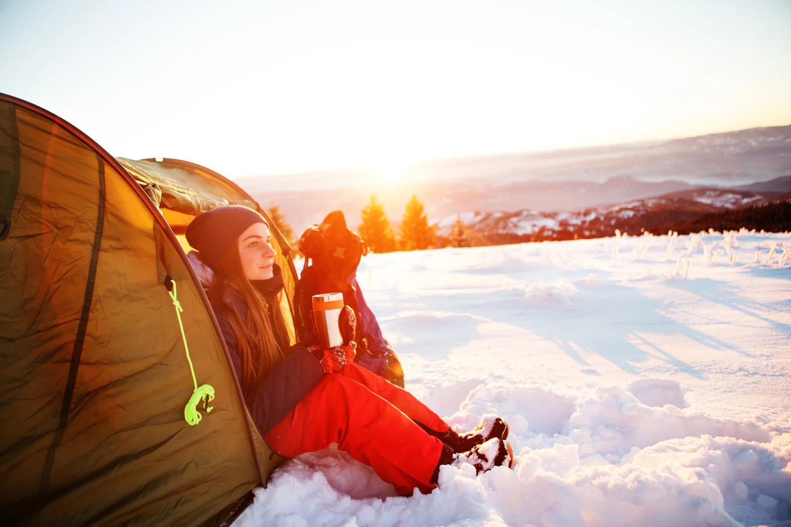Woman camping in the snow at sunrise, symbolizing peaceful winter camping adventures in state parks.