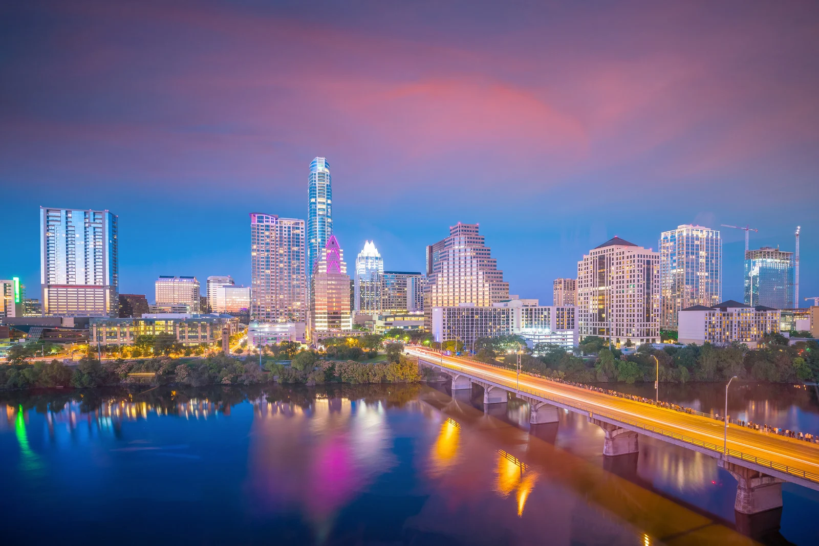 Austin city skyline at sunset with colorful lights reflecting on the water during a winter evening.