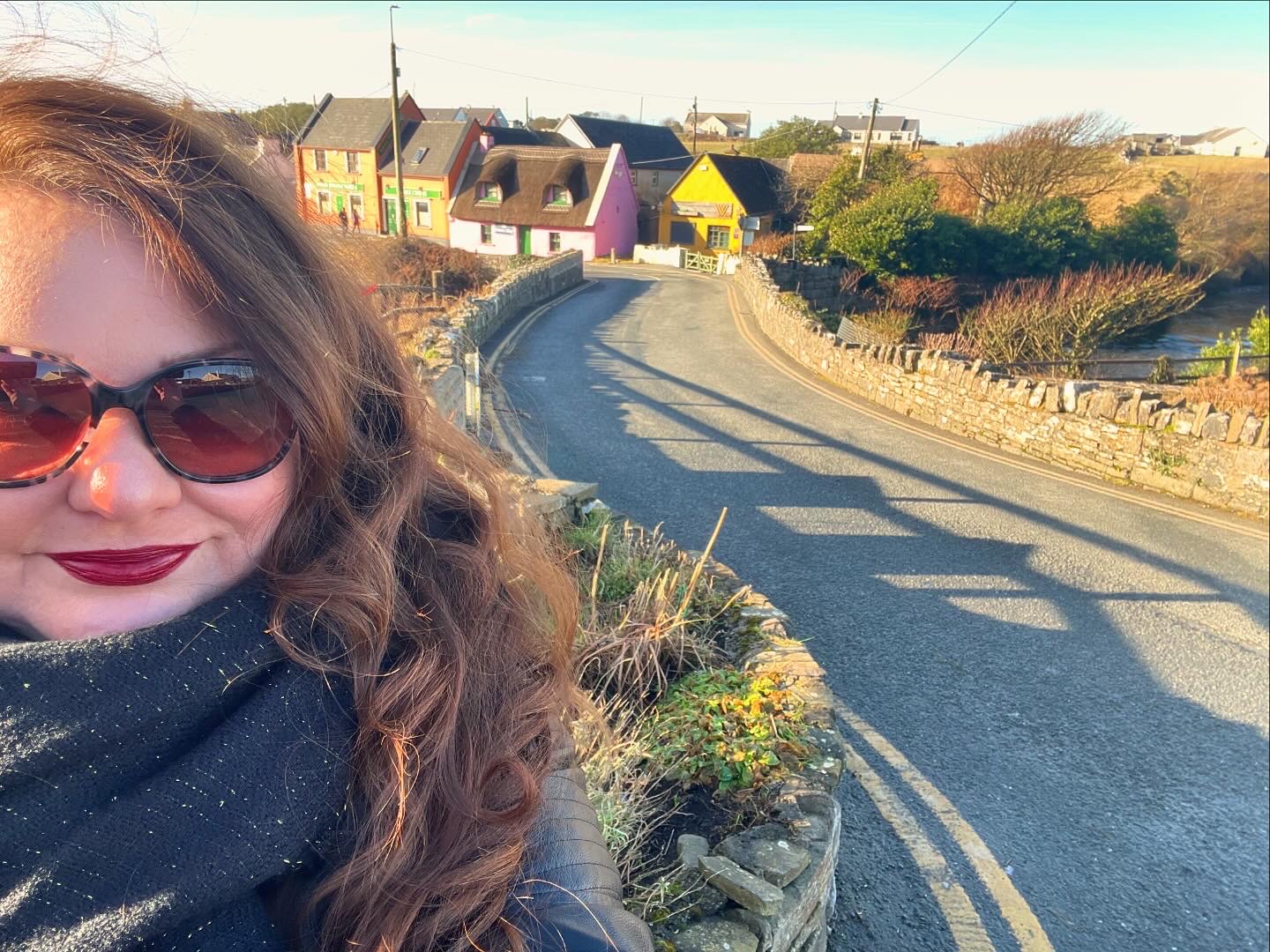 Woman on a solo road trip standing in front of colorful Irish village cottages along a winding country road.