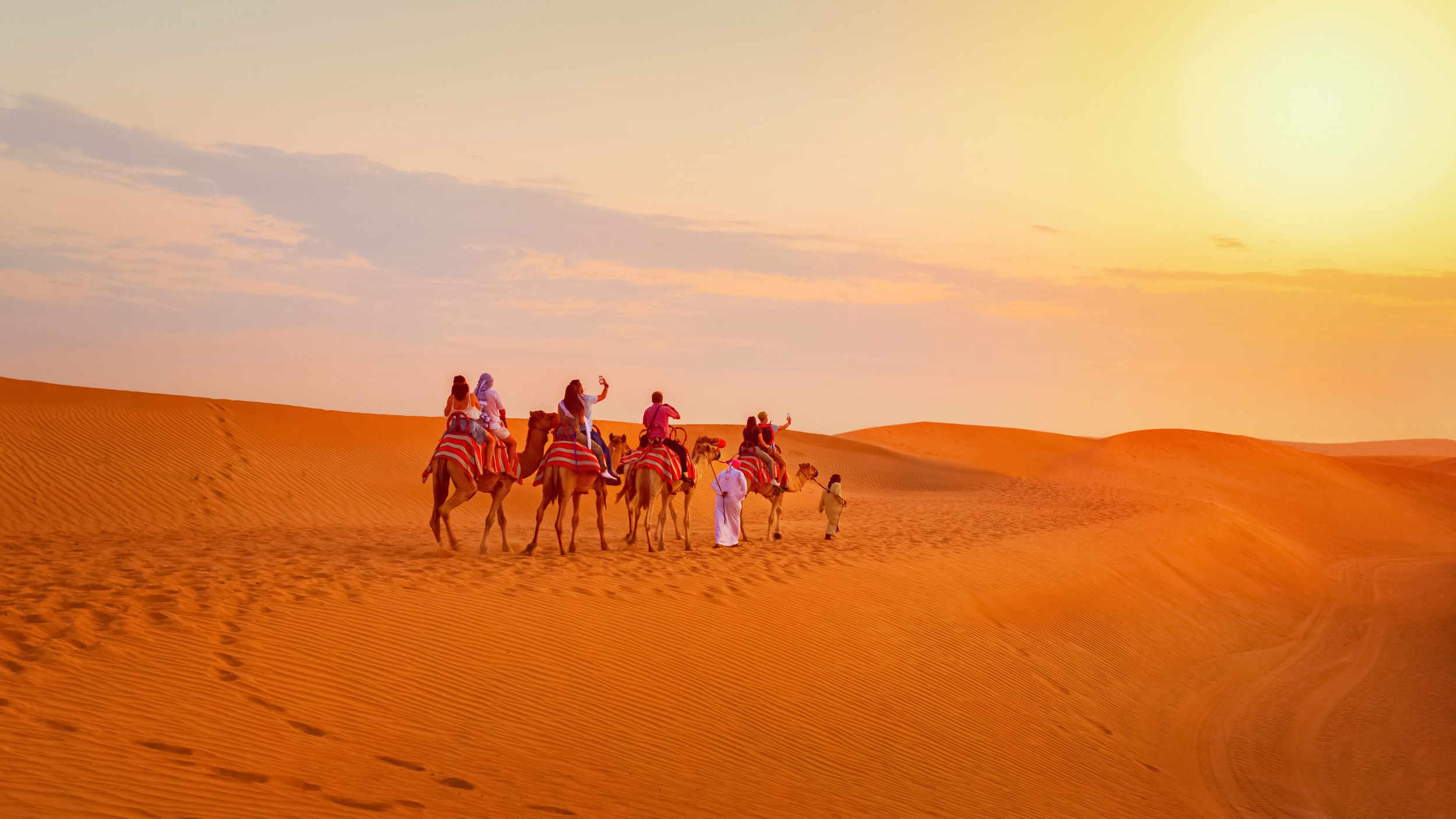 Caravan with group of tourists riding camels through Dubai desert during safari adventure
