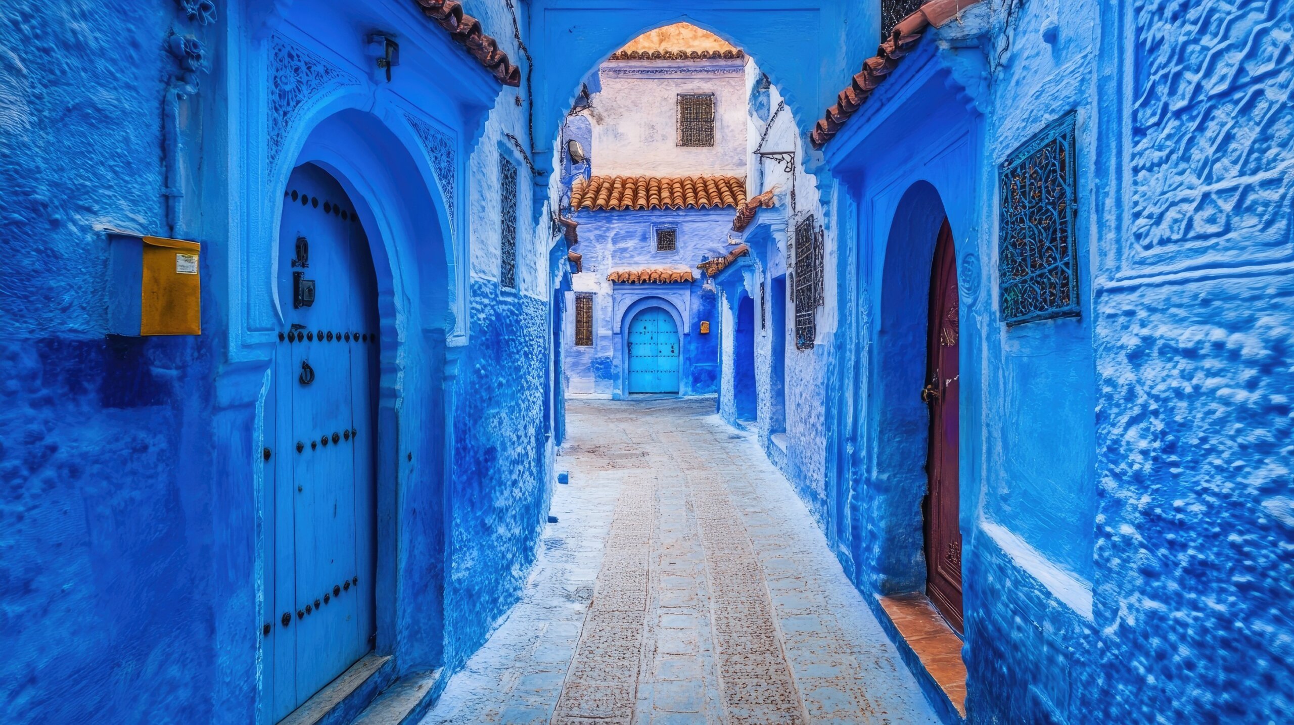 The iconic blue streets of Chefchaouen, Morocco, with narrow alleyways and traditional Moroccan doors framed by vibrant blue walls.
