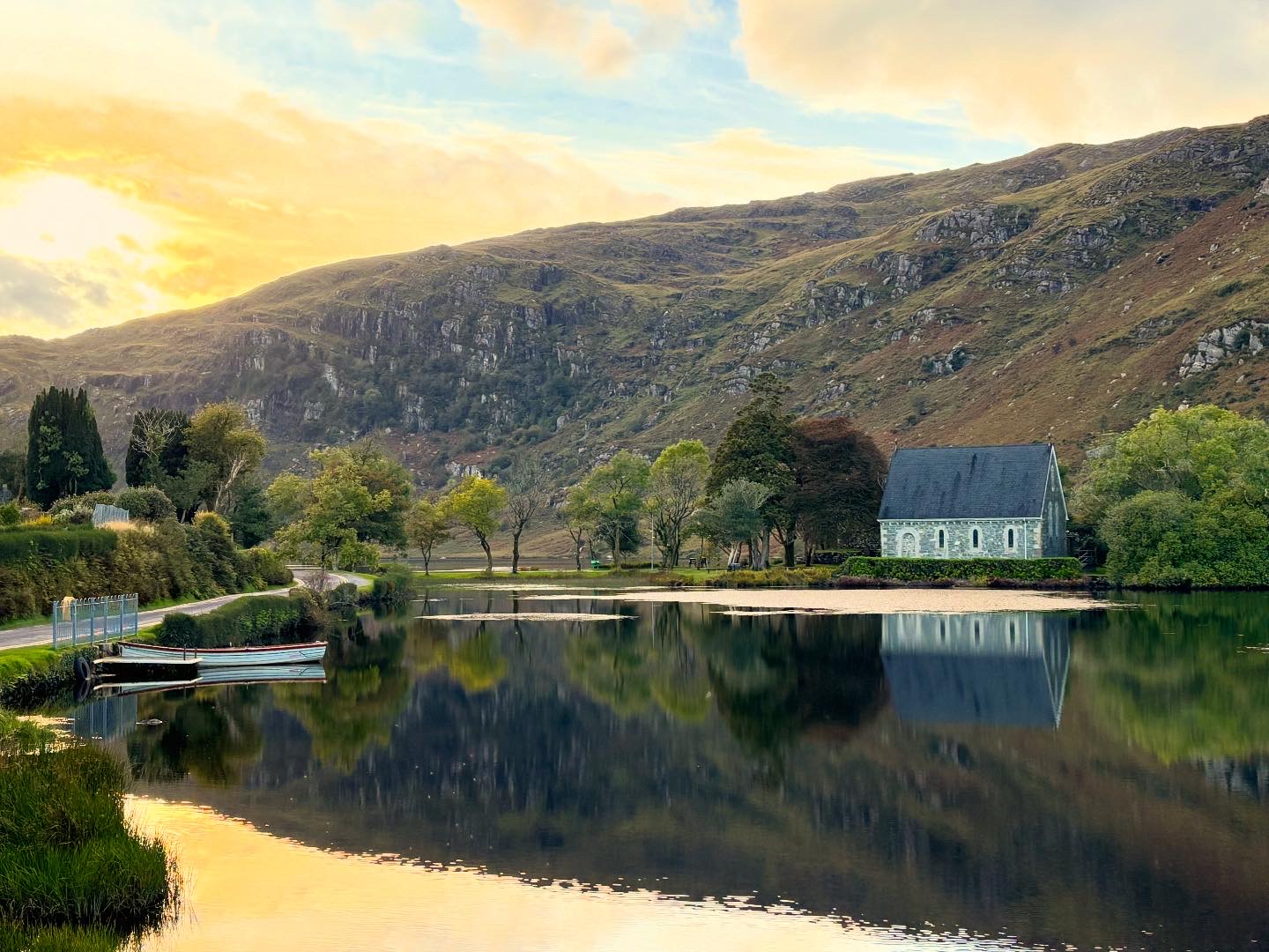 Winter sunrise at Gougane Barra with chapel reflected in a still lake surrounded by Irish mountains.