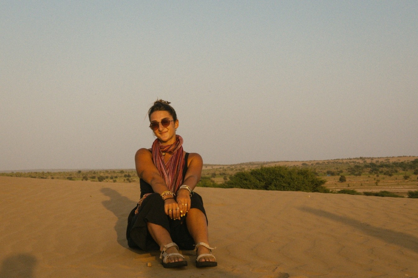 Solo female traveler sitting on sand dunes in India at sunset.