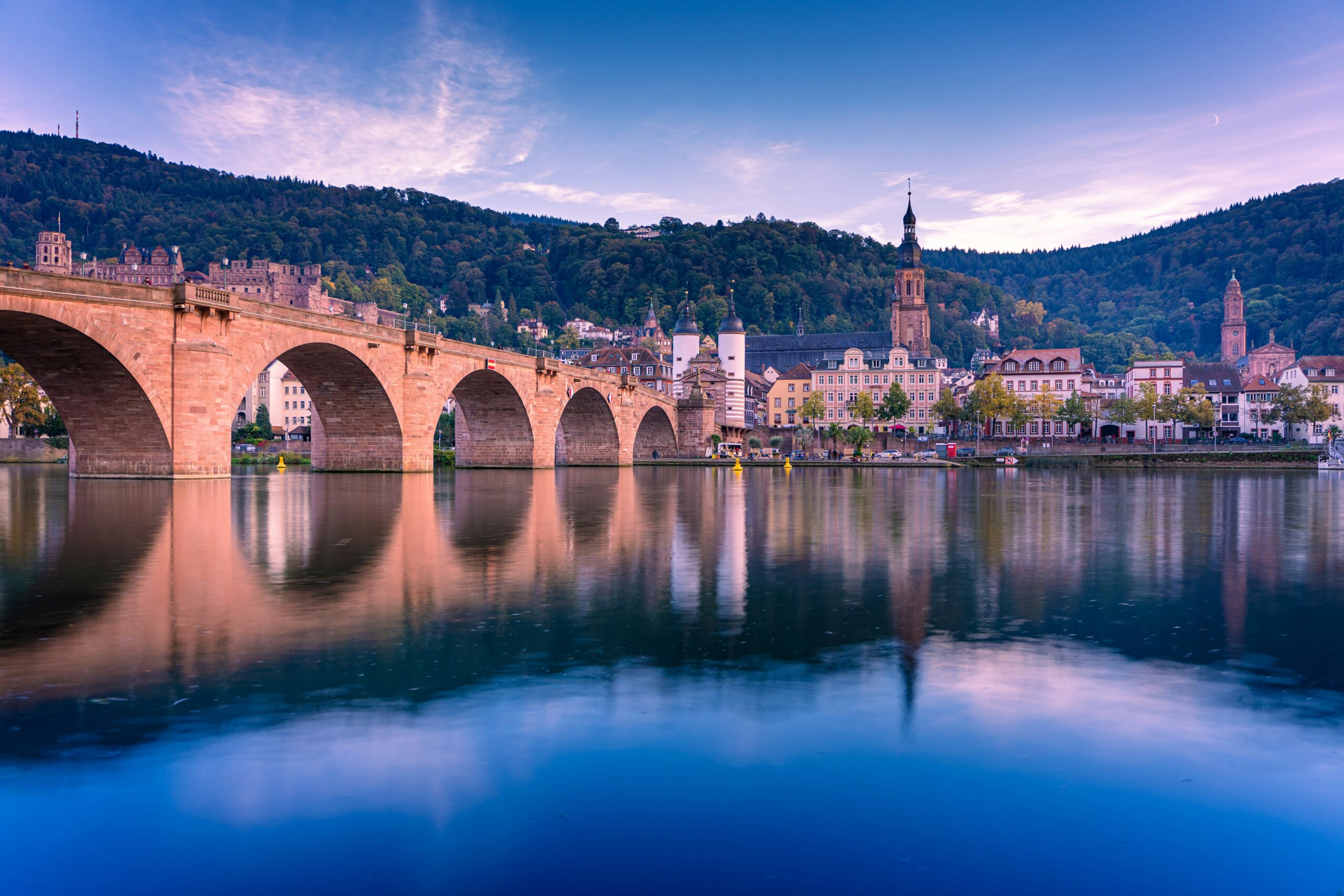Heidelberg Old Bridge at sunrise reflecting on the Neckar River, showcasing a peaceful European travel destination.