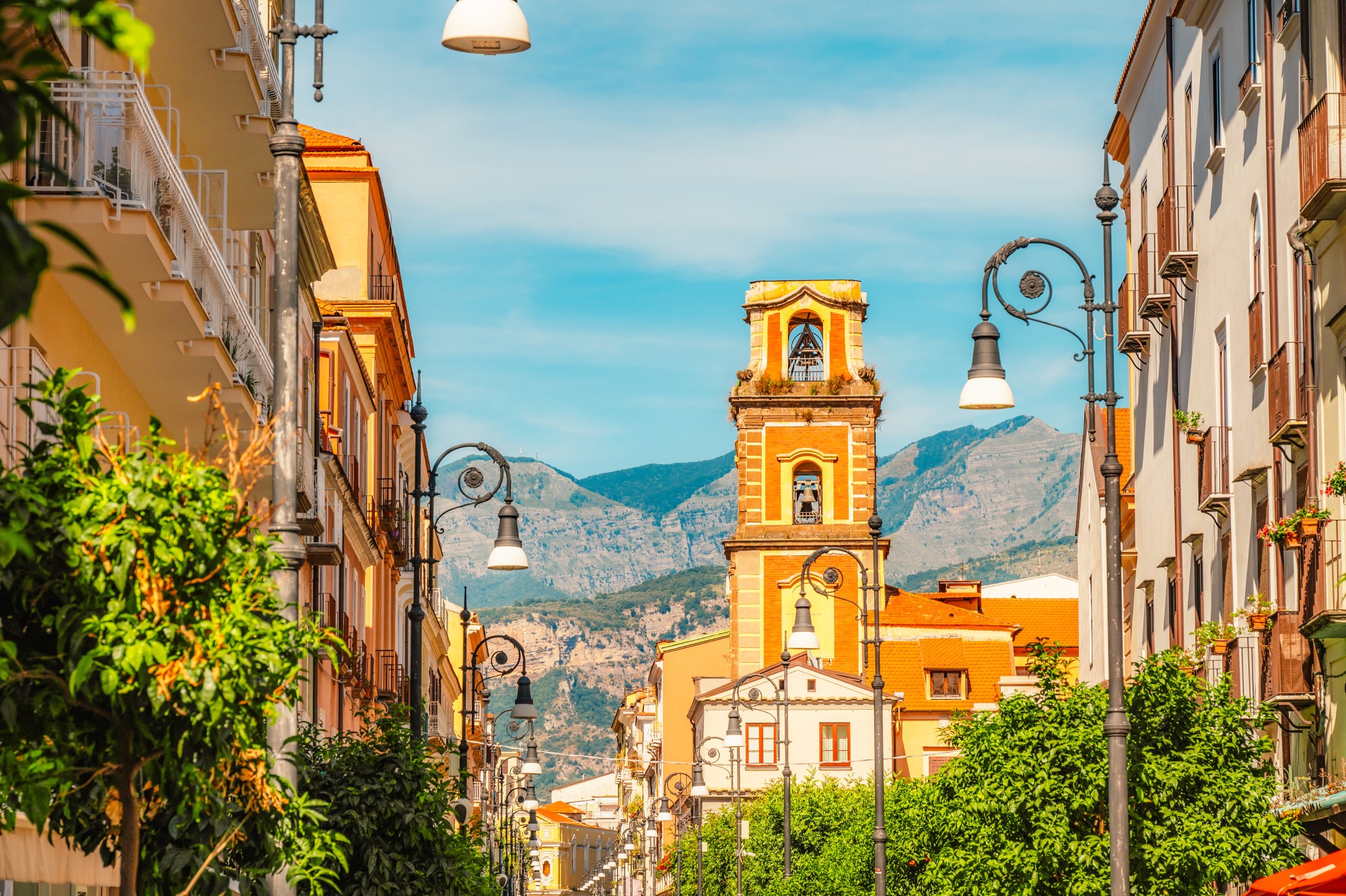 Colorful European street with church tower and mountains on a sunny day