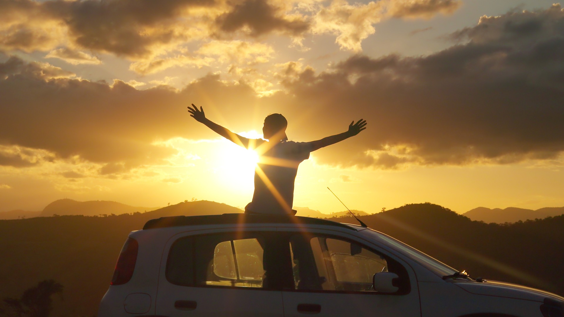 Happy and free man standing through a car sunroof at golden hour, arms open to the sky. Concept of freedom, gratitude, road trip, slow travel, mindfulness, and joyful lifestyle. 