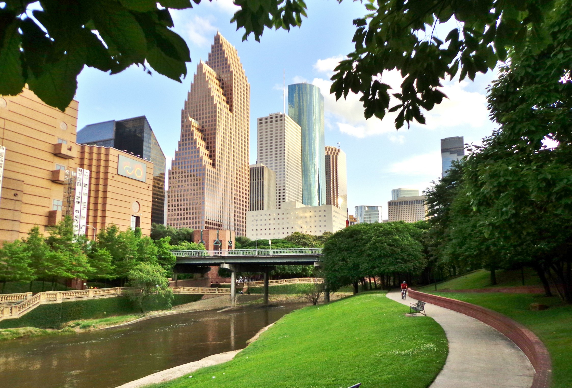 Bicyclist on Paved Bike Path in Buffalo Bayou Park, with the Skyline of Downtown Houston in the Background - Houston, Texas, USA
