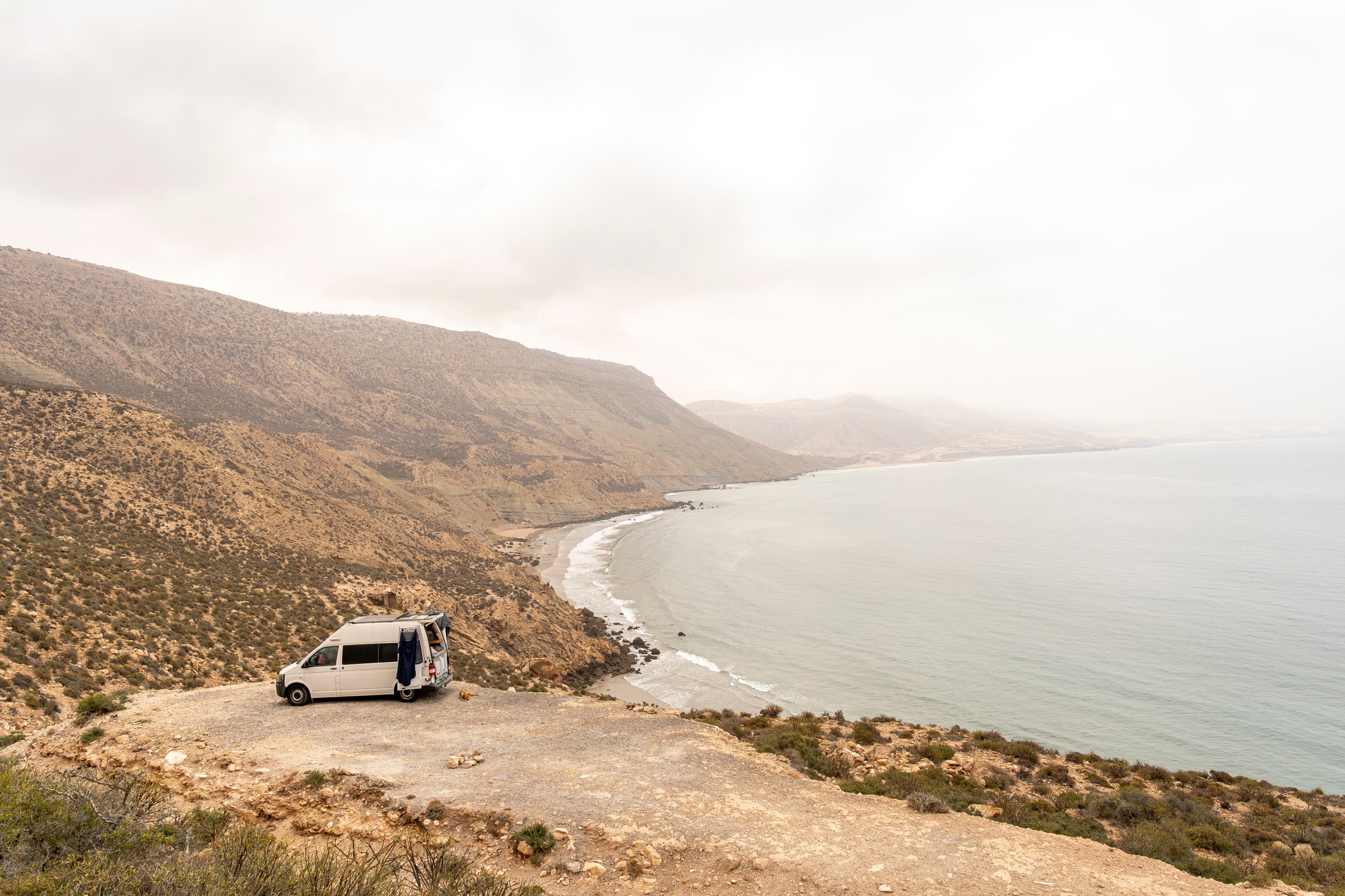 Travelling surfers camp in their van with a dog , campfire and wetsuit, overlooking imsouane, near Tagazout, Agadir, Morocco.