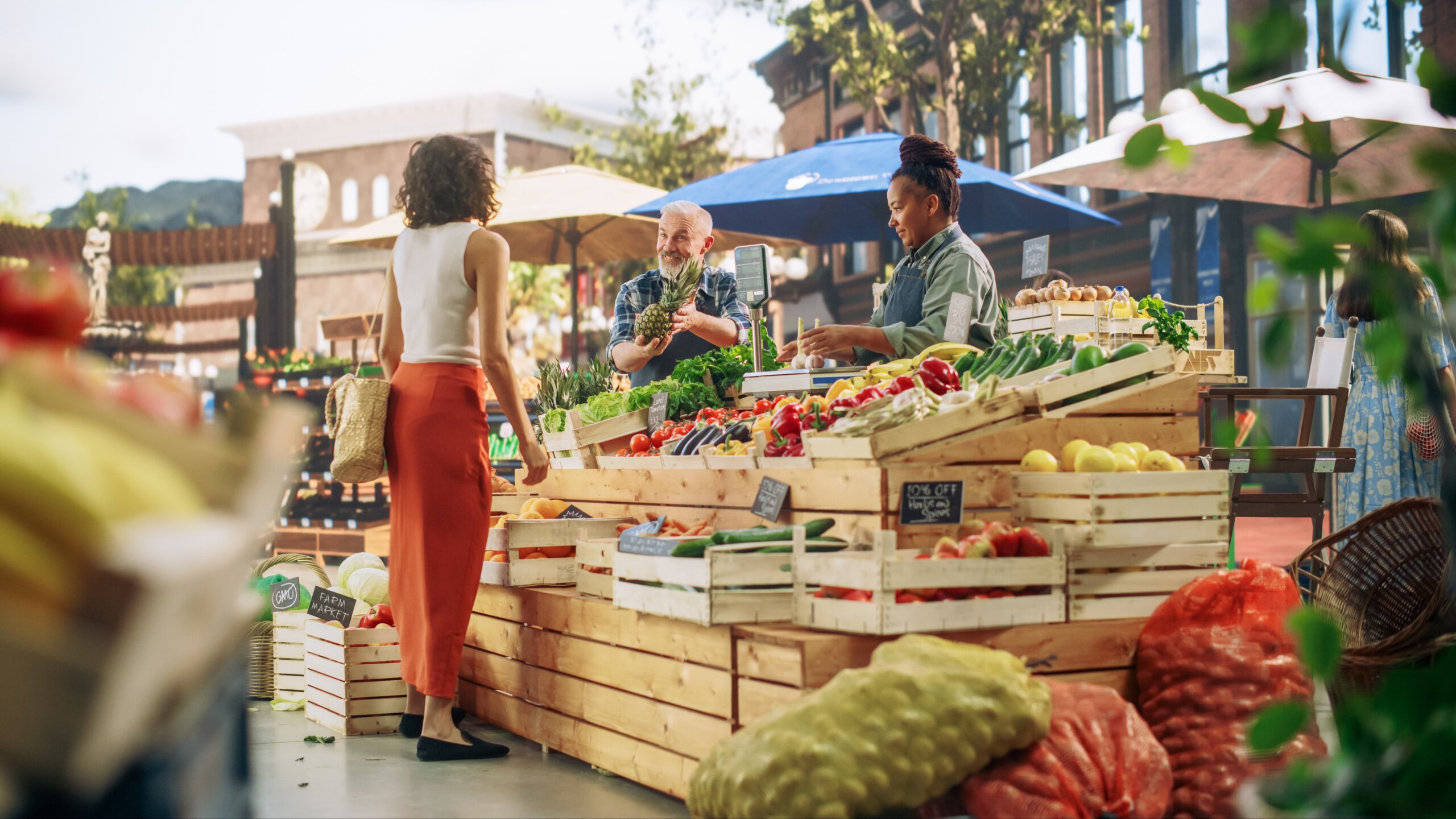 Hispanic Female Customer Buying Two Garlic Heads and a Pineapple From a Multiethnic Farmers Couple. Successful Adults Managing Small Business Farm Stall at a City Square Market