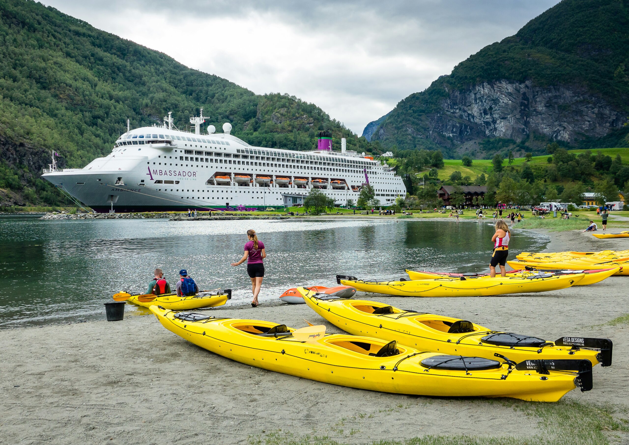 Cruise ship in a fjord near kayaks on shore, showing why travel by cruise ship makes sense for visiting remote destinations and multiple ports