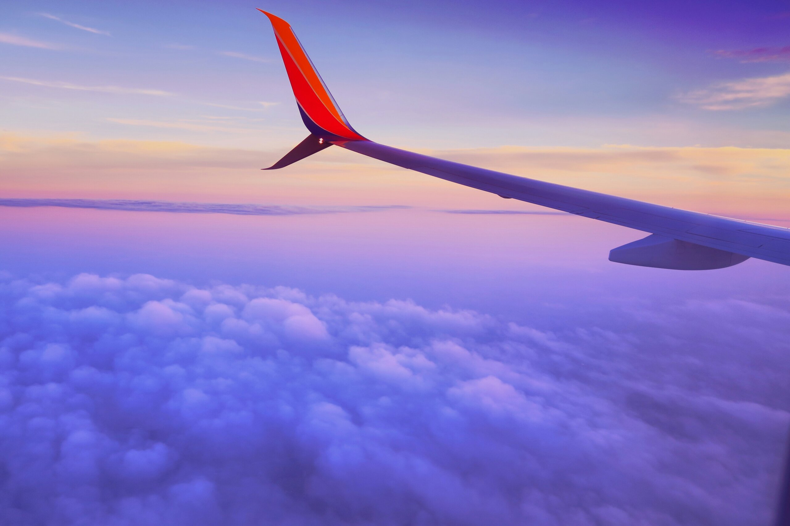 Red airplane wing above clouds at sunset viewed from passenger window seat