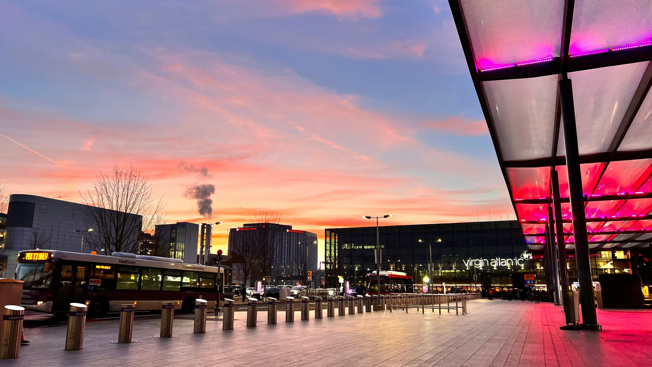 Modern airport terminal exterior at sunset with pink LED lights buses and ground transportation
