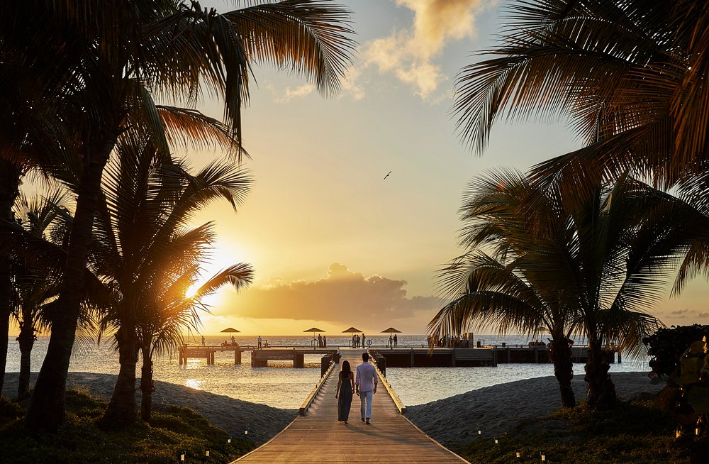 Couple walking on a sunset boardwalk at a tropical wellness retreat, representing restorative travel for mind and body