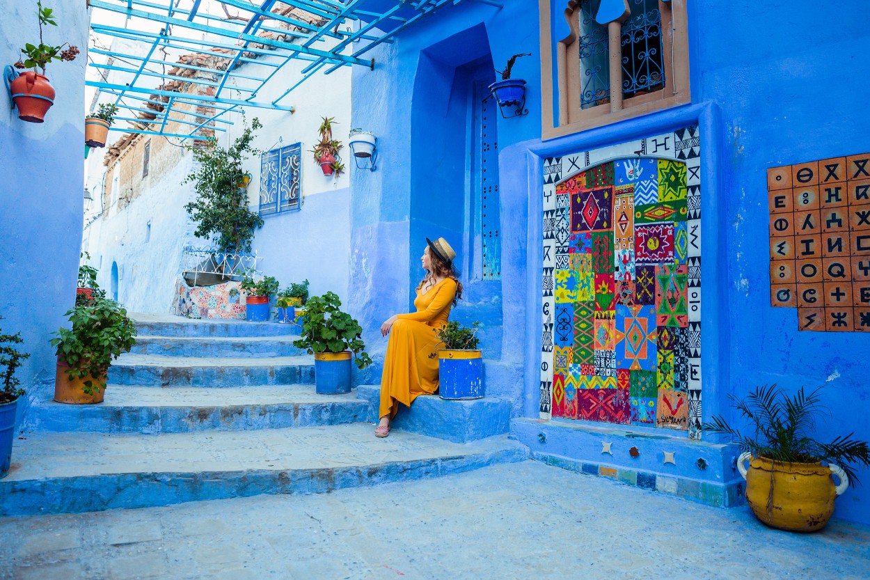 Beautiful caucasian woman in a yellow dress and a boater hat posing in a blue city in Morocco. Chefchaouen.

