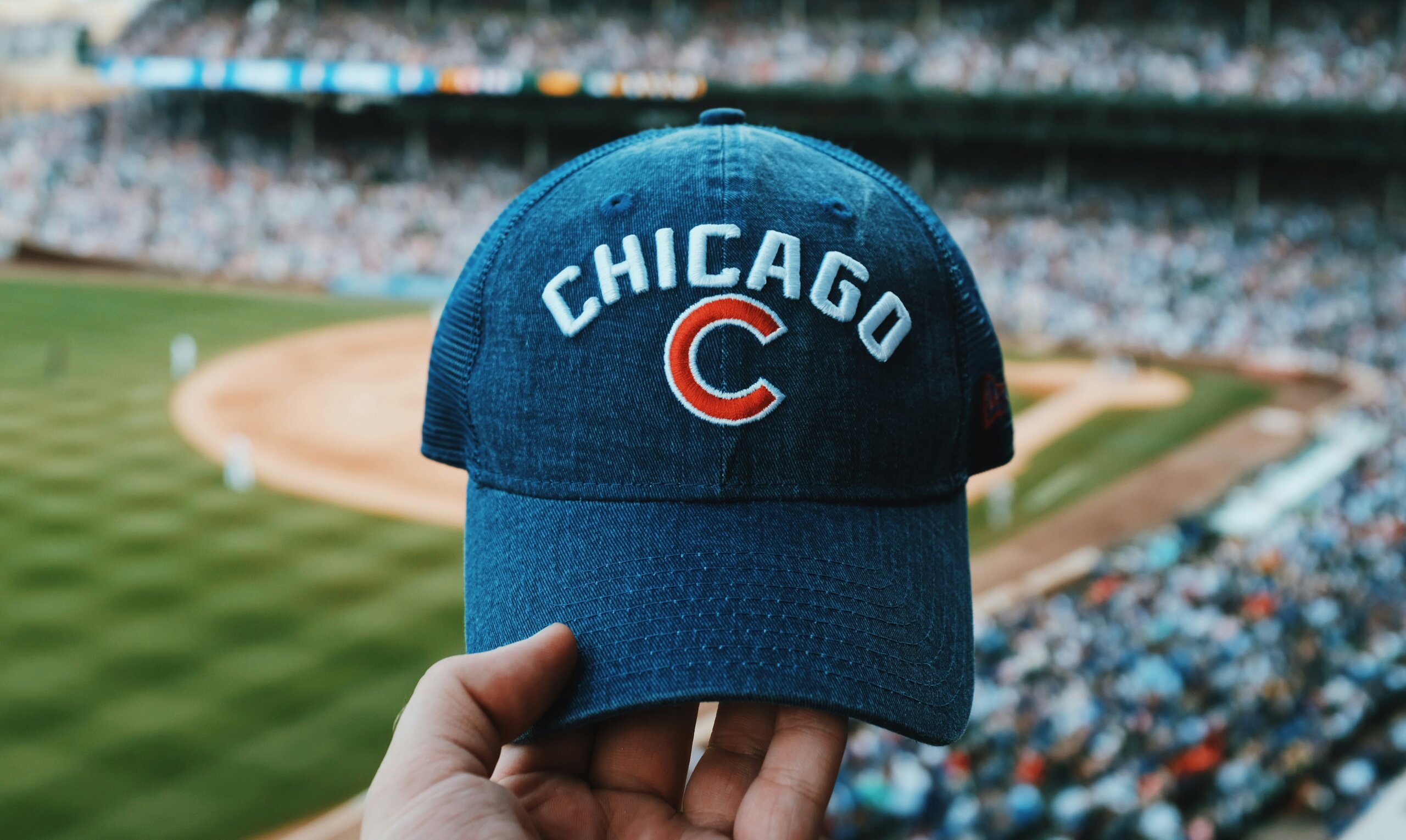 Hand holding a Chicago baseball cap at a stadium, a common accessory that can scream American tourist while traveling