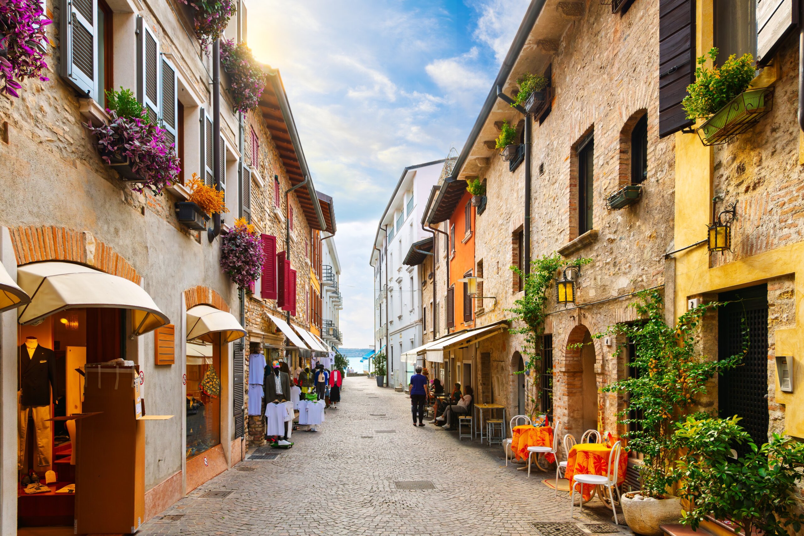 A narrow cobblestone pedestrian street leading with views of Lake Garda in the historic medieval town of Sirmione, Italy.