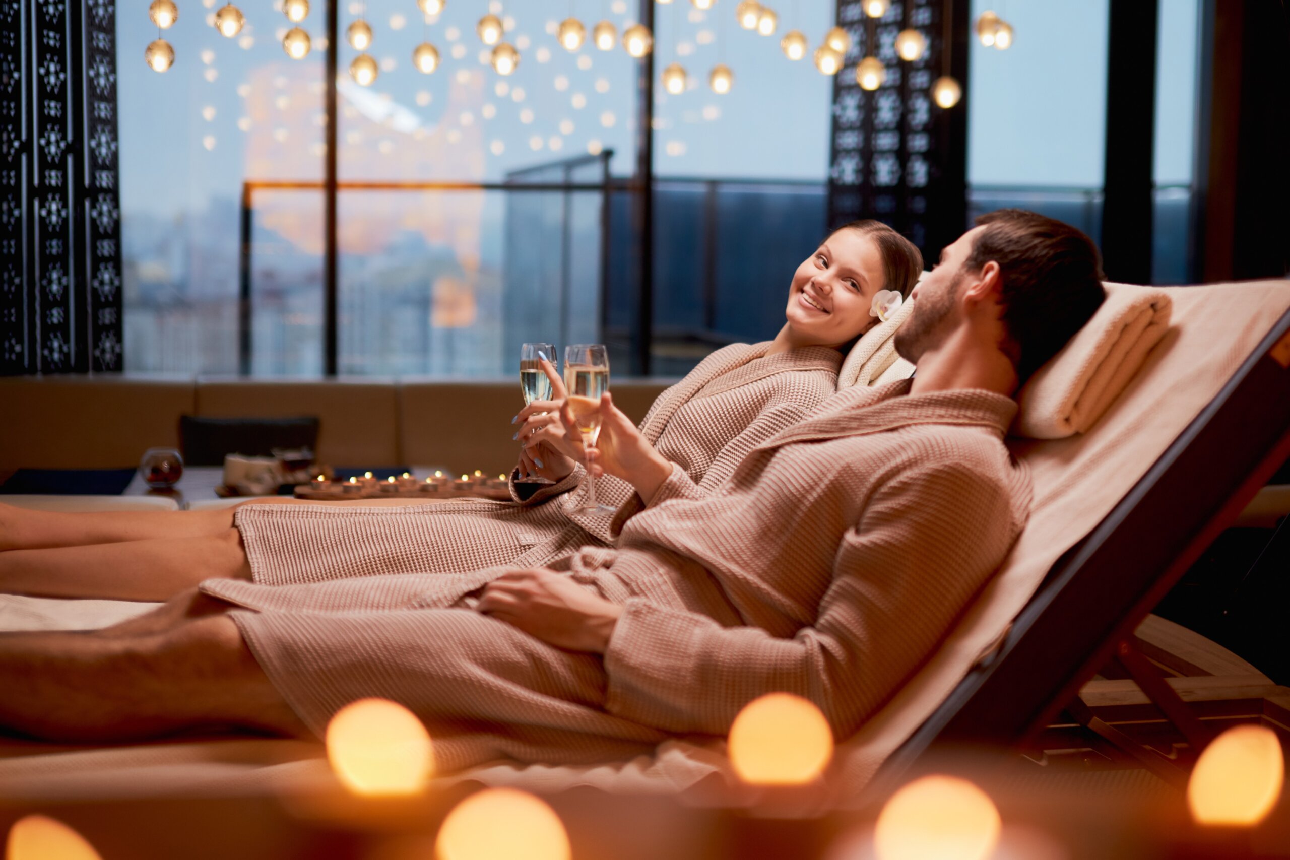 Spa, relax, enjoying concept. Married couple together relaxing in spa salon, lying on beds drinking champagne, using candles
