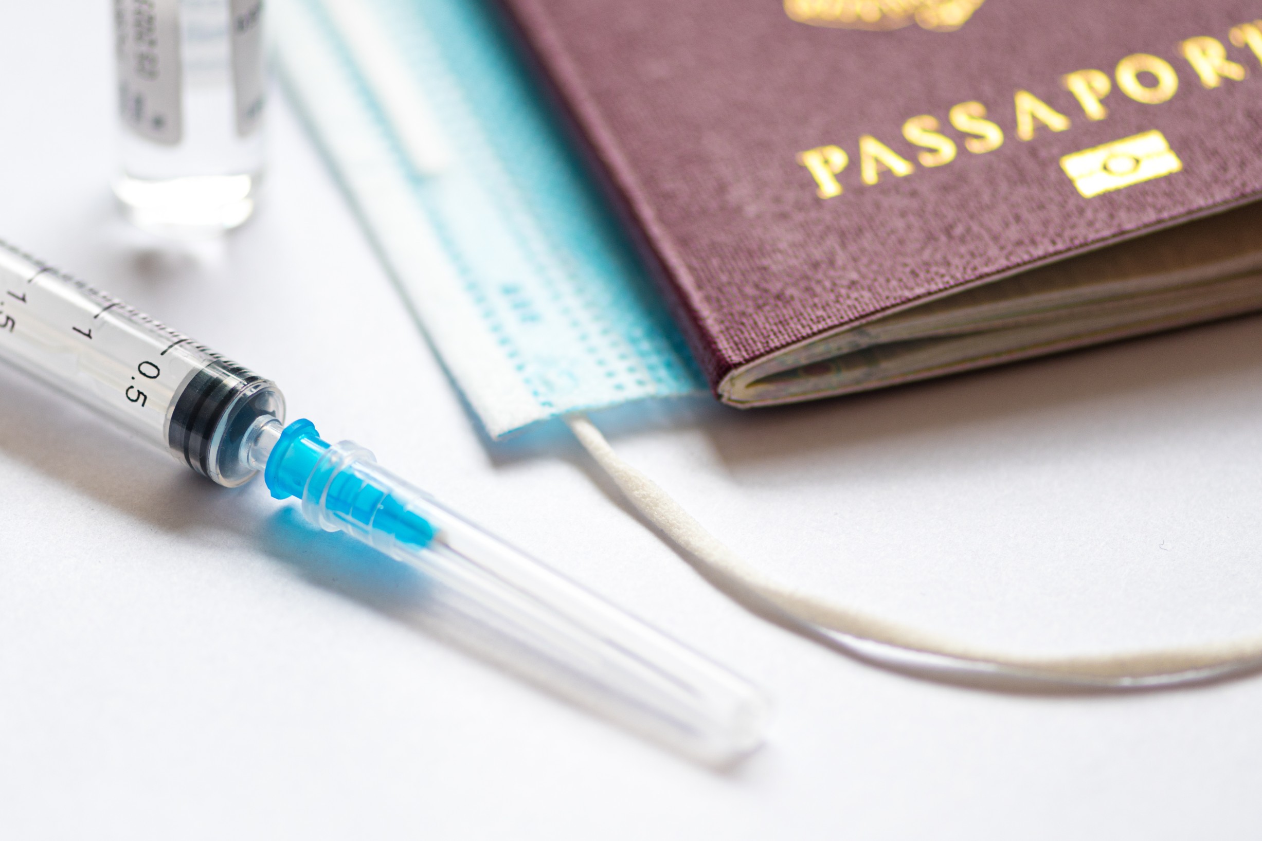 Syringe with needle, vial, surgical face mask and passport or visa on a white table ready to be used. Covid or Coronavirus vaccine
