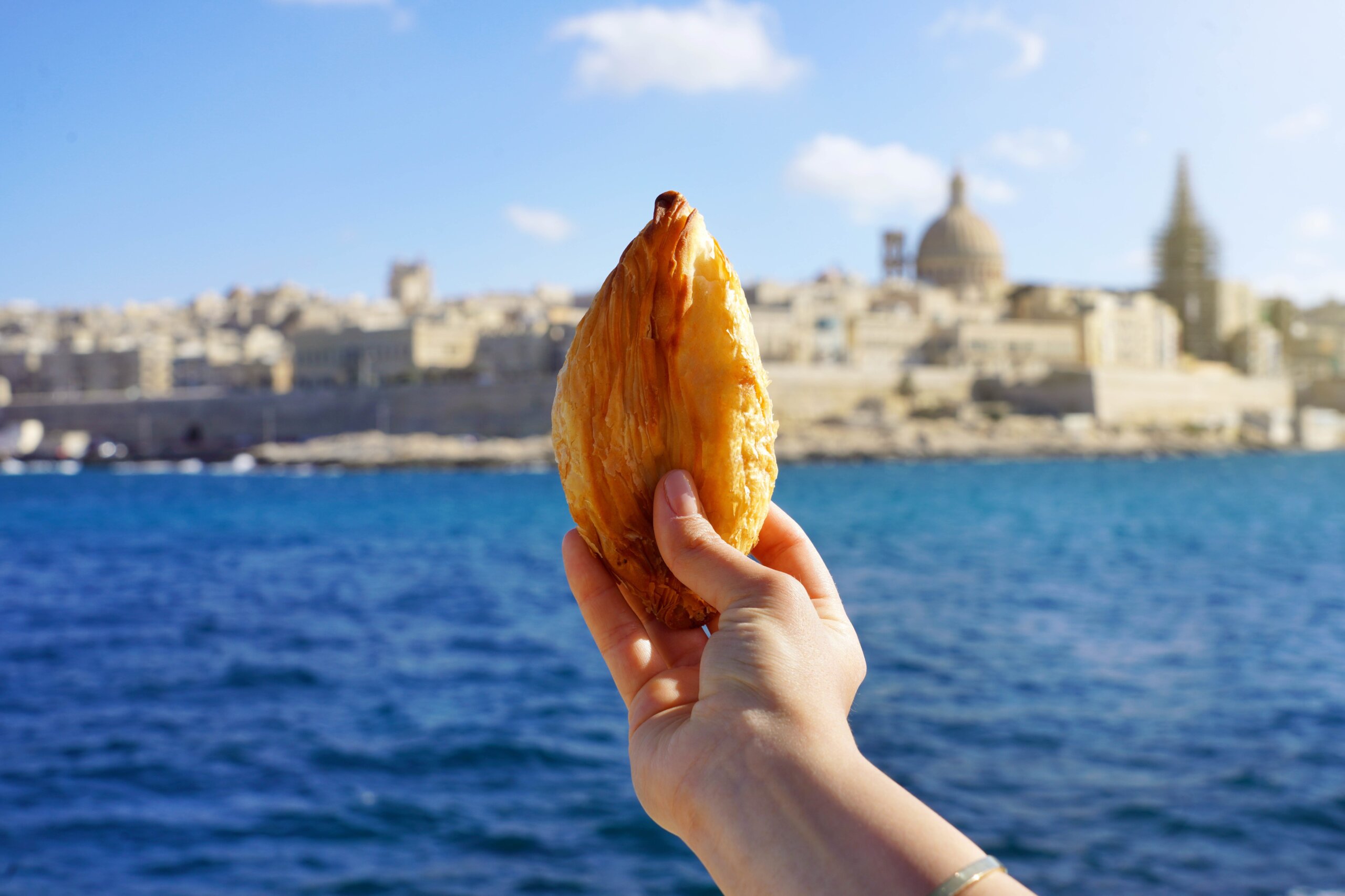 Traditional Maltese pastizzi pastry held over Valletta waterfront in Malta