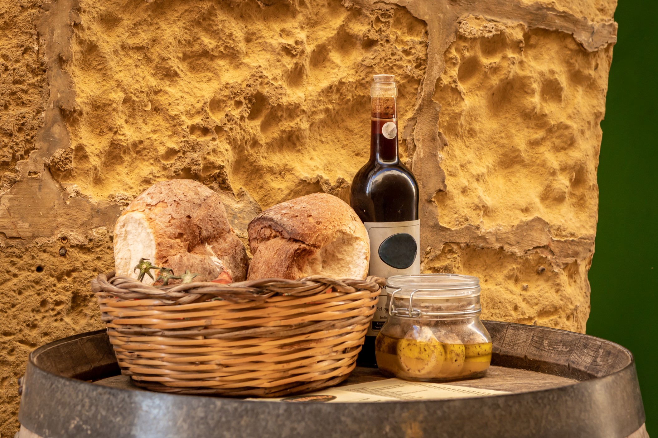 Bottle of wine, artisan bread in wicker basket and marinated cheese in a jar on a wooden barrel. Traditional  food products of Malta.

