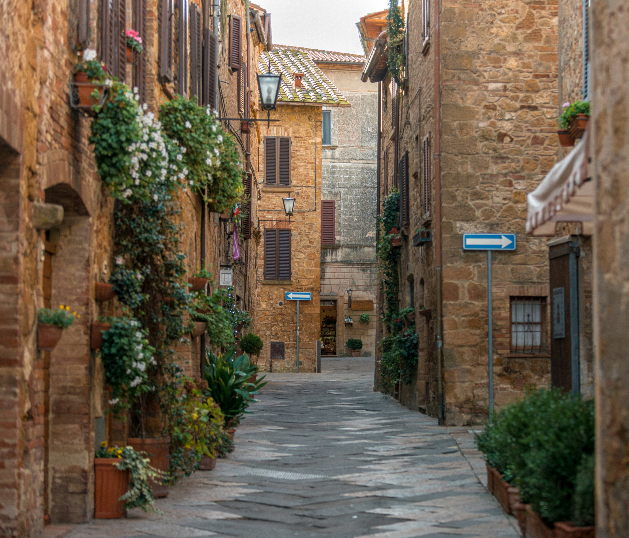 pienza, italy - Narrow cobblestone alley lined with stone buildings and flowering vines in a quiet Italian hill town, representing slow travel in Europe.