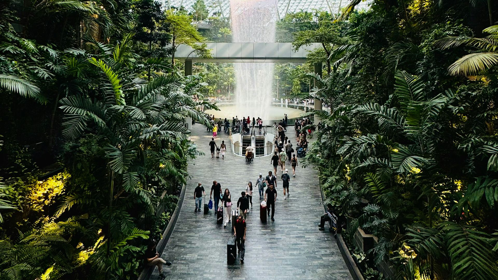 airport terminal with indoor waterfall tropical garden and travelers walking below