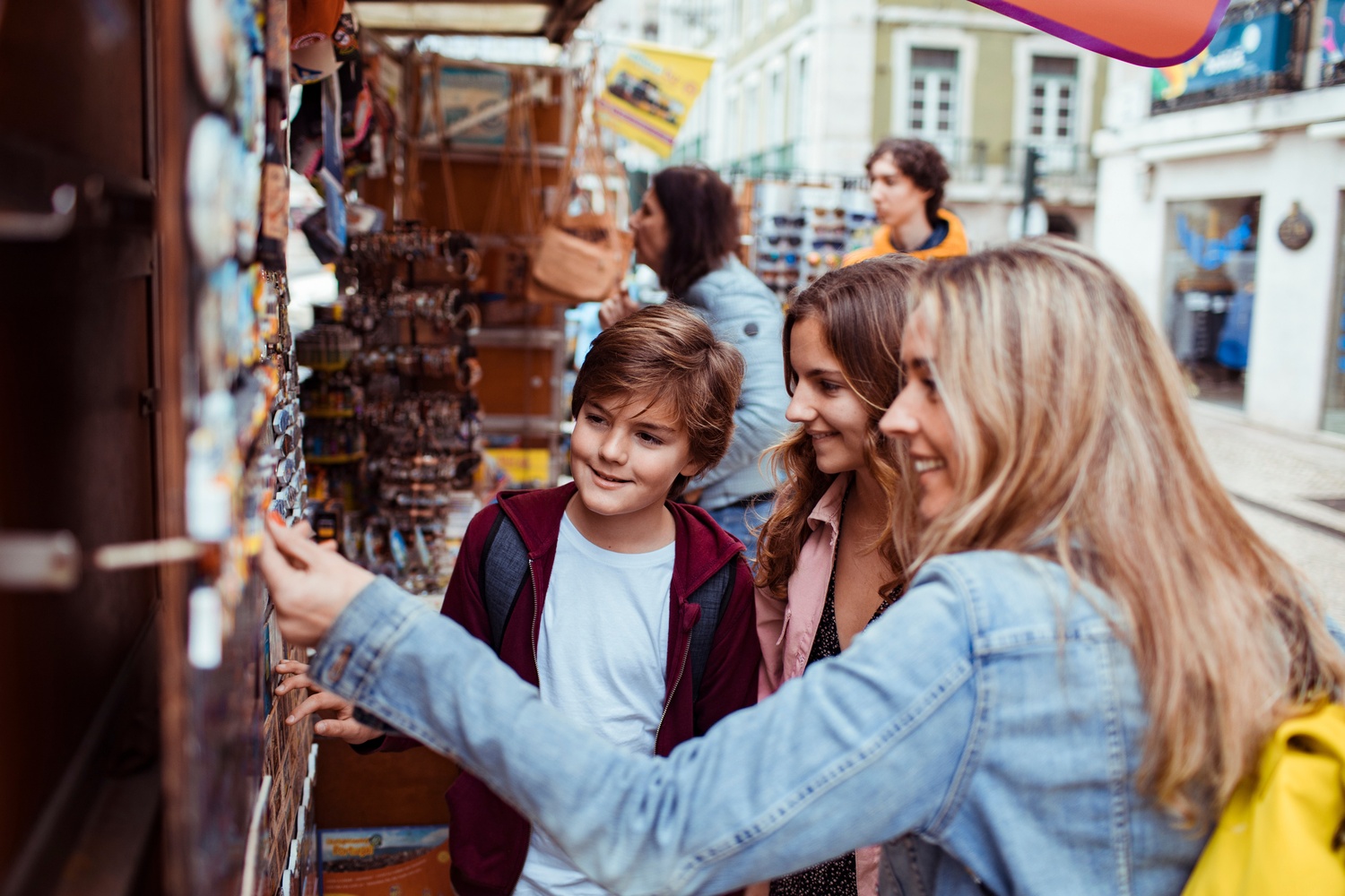 Woman and two kids browsing handmade souvenirs at a colorful outdoor street market stall while traveling