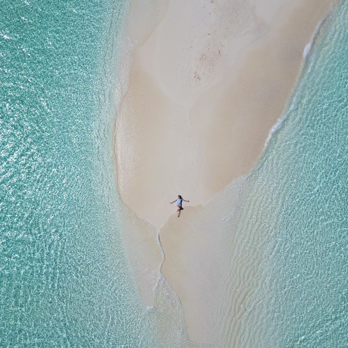 Woman enjoys the crystal-clear water of Maldives by laying on the sandbank in the middle of nowhere
