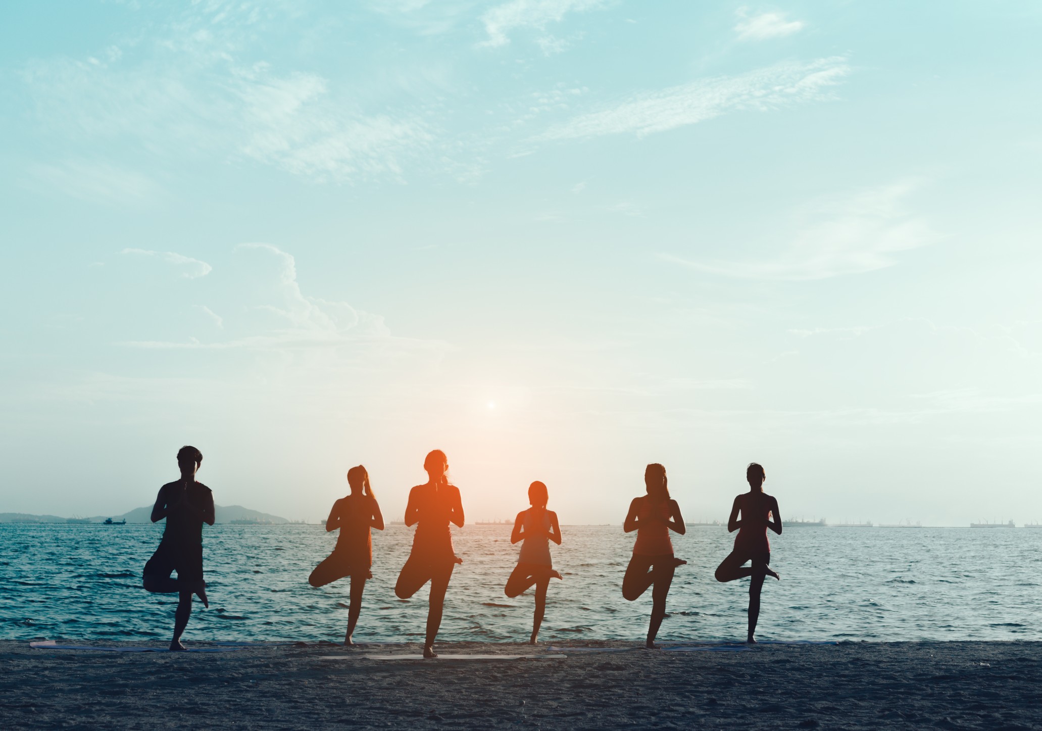 Young group man and woman yoga practice on mat relaxation in class exercise with pose fitness sport for healthy on the beach and seaside modern city at sunrise relax holiday vacation time in summer. 