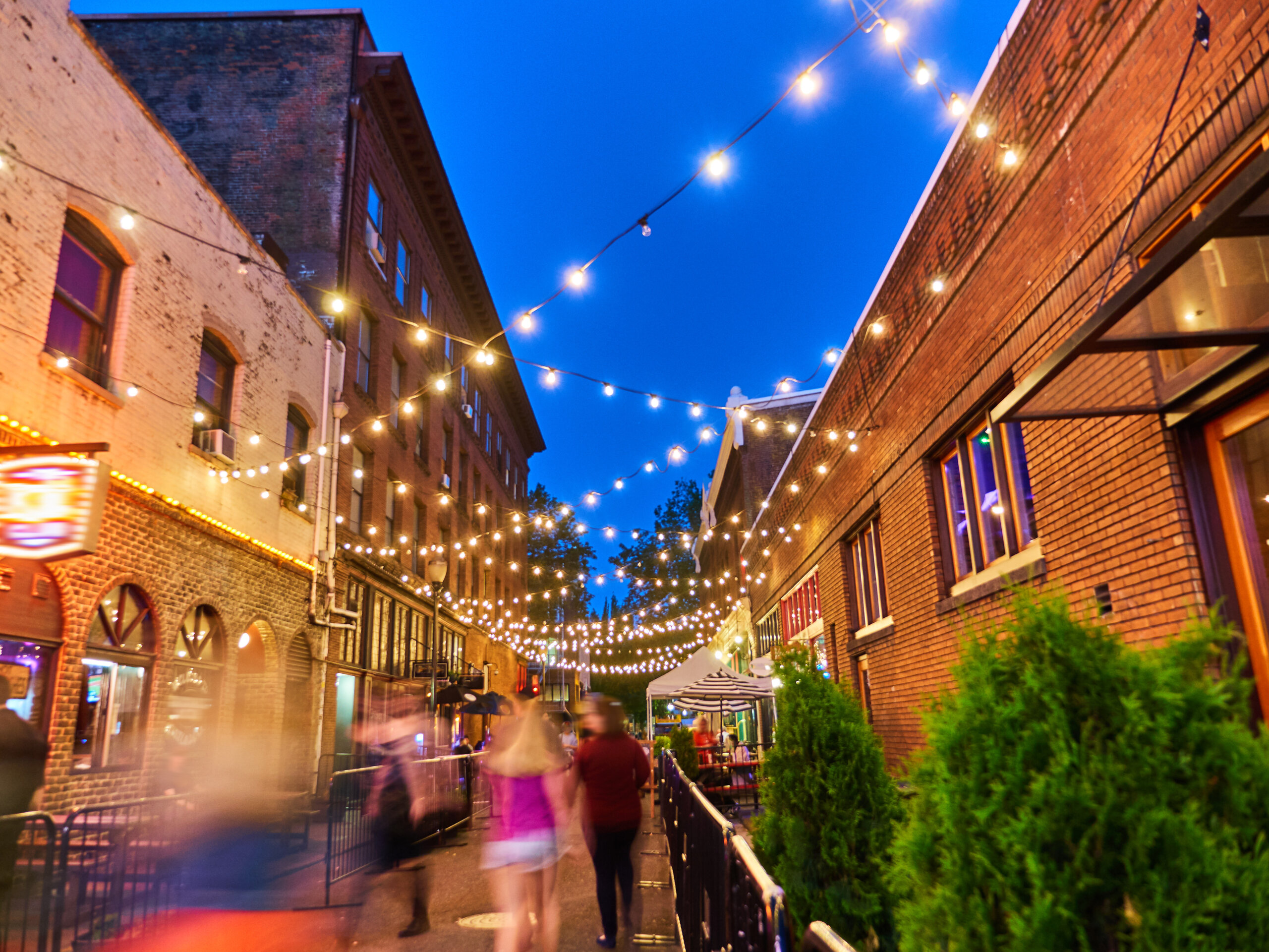 city street at night with string lights people walking and outdoor dining atmosphere