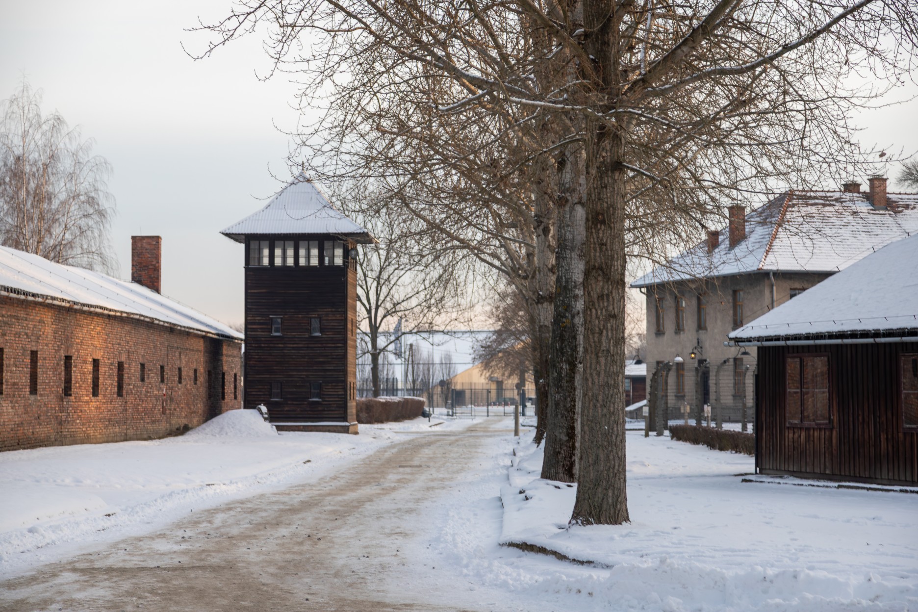 OSWIECIM, POLAND - JANUARY 5, 2025: A watchtower and brick barracks at the Auschwitz I Nazi concentration camp memorial and museum covered in snow during winter.