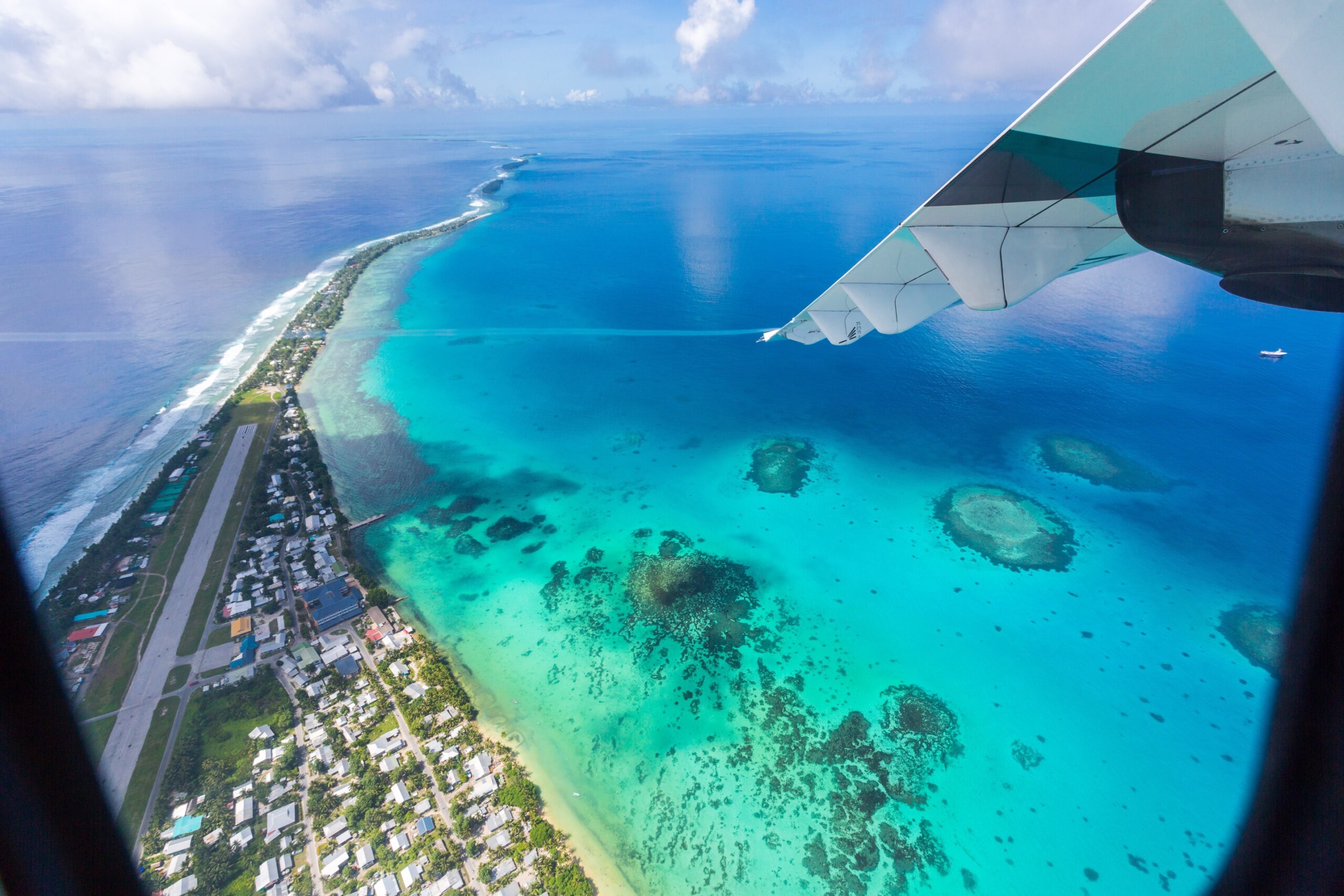 Tuvalu lagoon under wing of an airplane. Aerial view of Funafuti atoll and the airstrip of International airport in Vaiaku. Fongafale motu. Island nation in Polynesia, South Pacific Ocean, Oceania