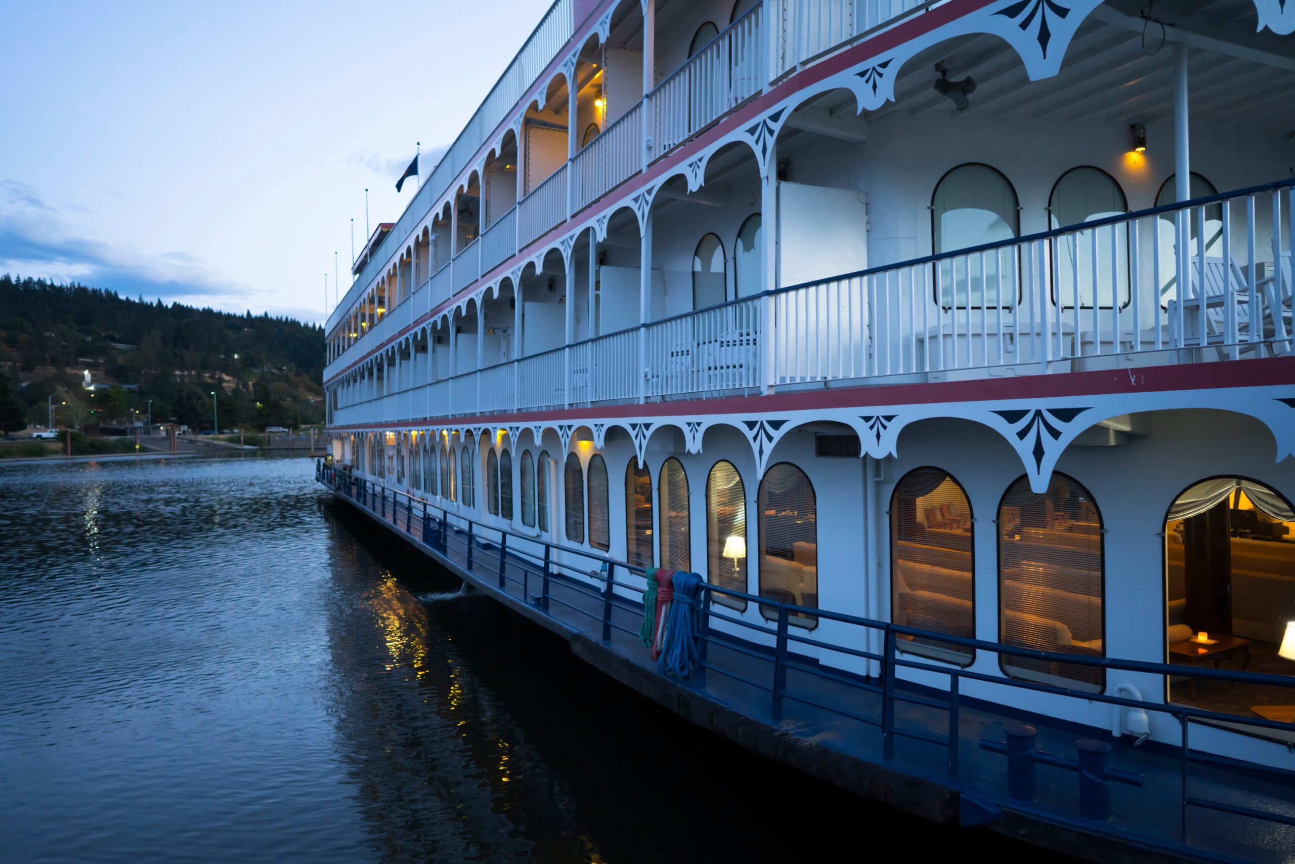 Three-deck cruise ship with lights in the cabins moored at the pier on the Columbia River
