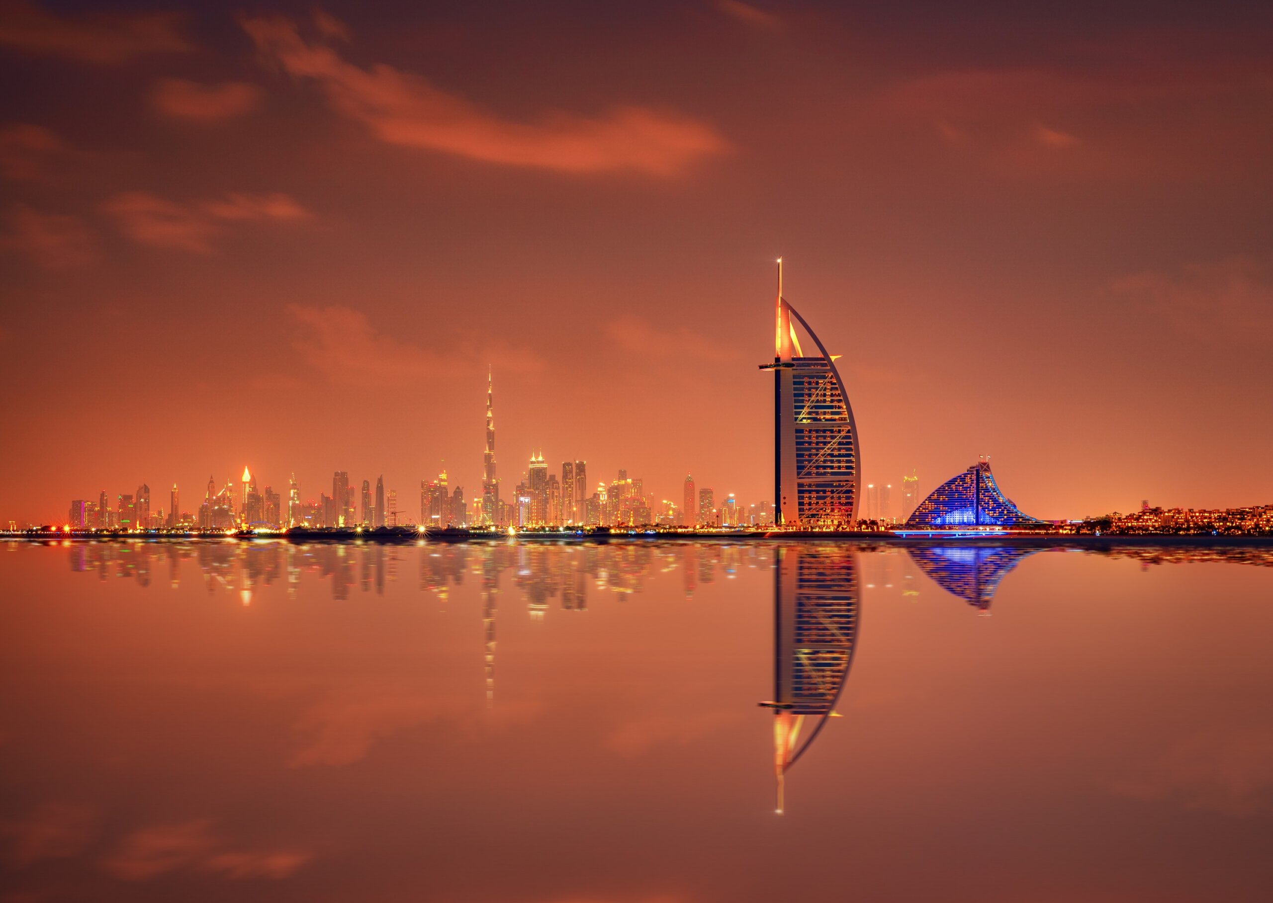 Dubai skyline at night with Burj Al Arab and city lights reflected on the water