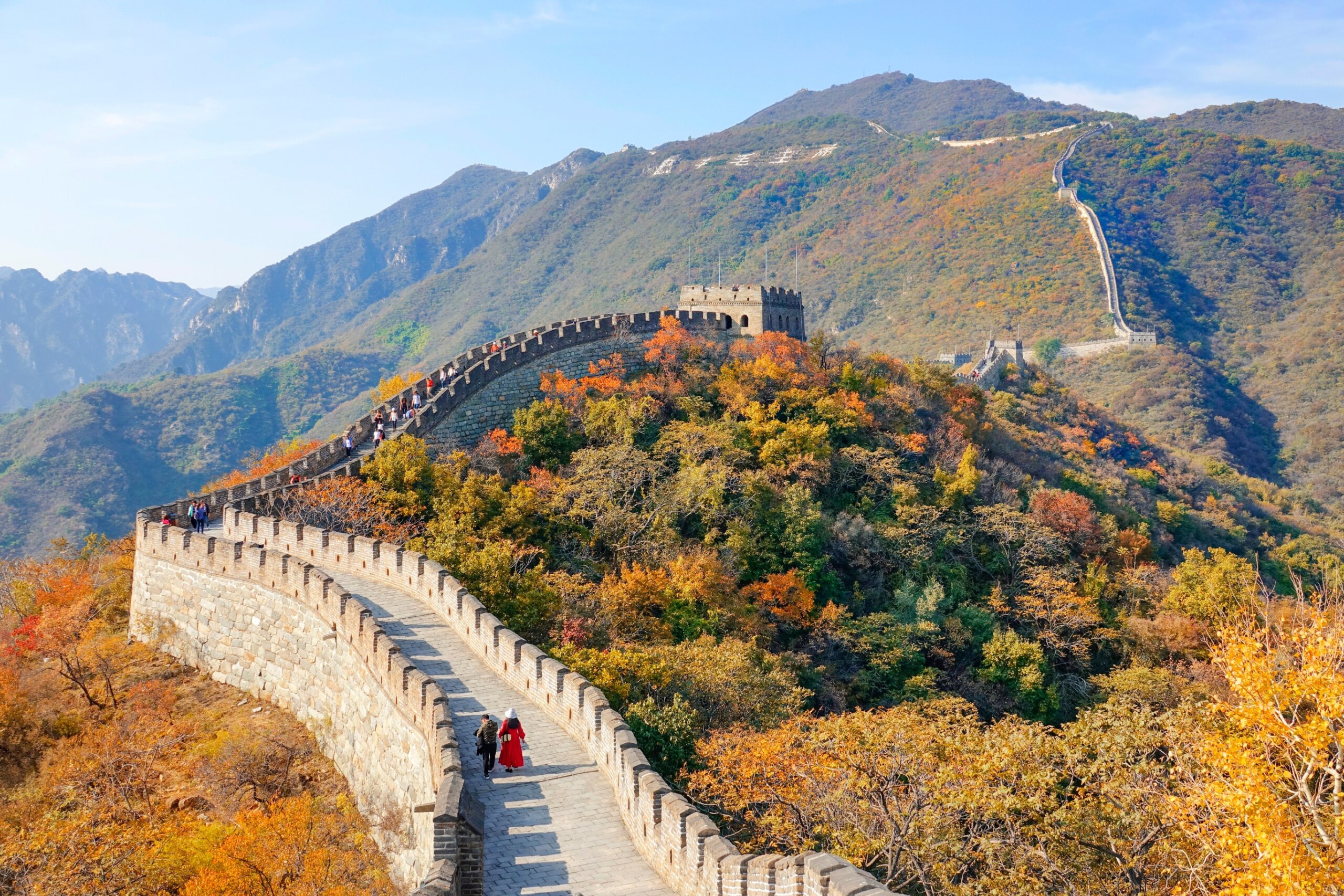 Two unrecognizable tourists walk along the walkway atop the Great Wall of China.
