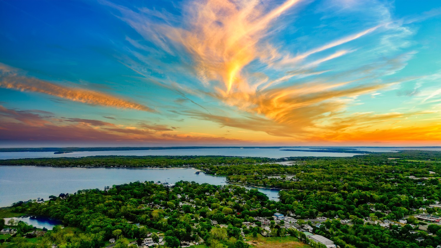 his breathtaking drone shot captures the serene beauty of Southold in The Hamptons, New York. As the sun sets, it casts a golden glow over the lush landscapes and the expansive waters of Peconic Bay.