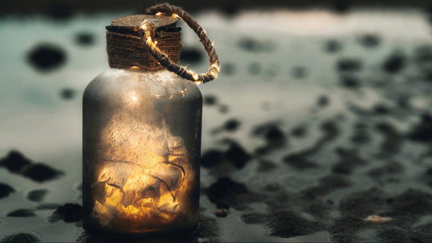 Glowing glass jar with fairy lights on dark wet stones, symbolising Scottish folklore and mystery