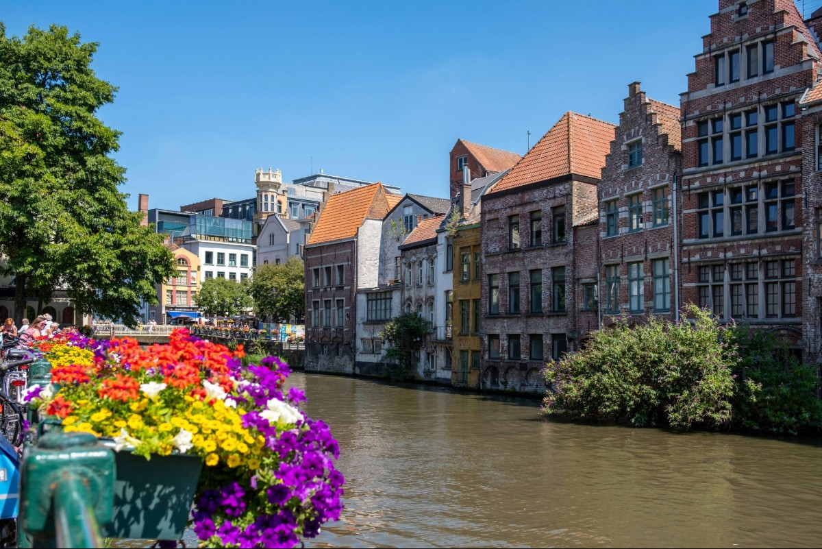 Colorful flower boxes along a sunny canal in Ghent Belgium with historic medieval guild houses lining the waterfront