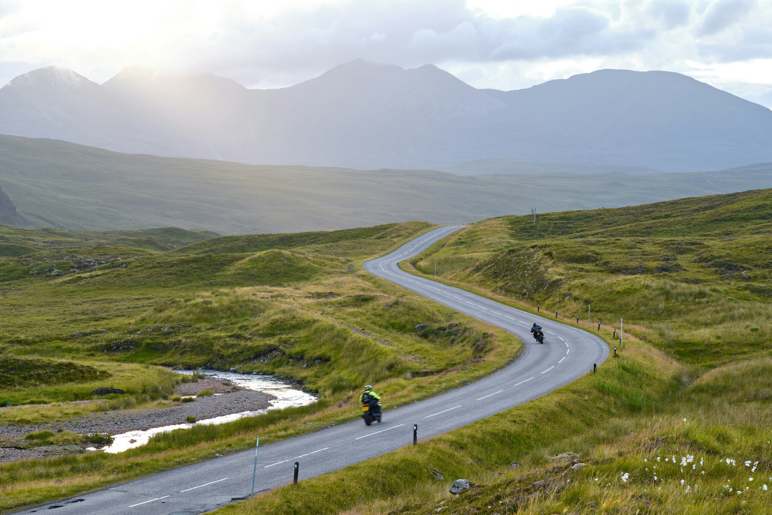 winding road through the Scottish Highlands with green hills and mountains in the background